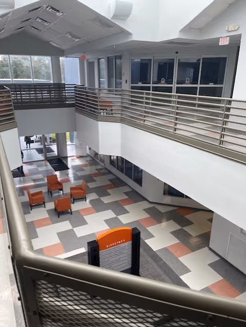 Atrium-style interior with a balcony railing, geometric tiled floor, and orange seating.