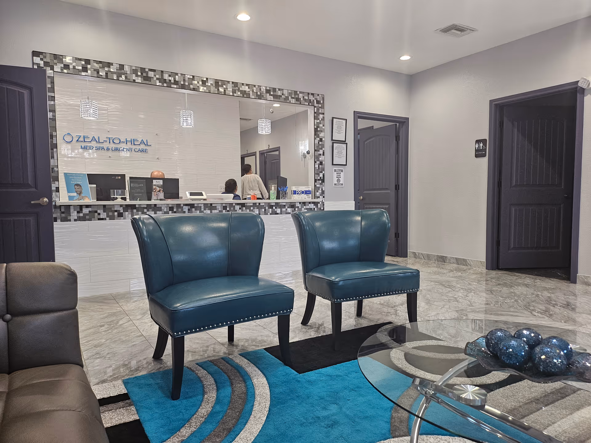 Lobby with teal chairs, glass coffee table, and mosaic-framed reception desk.