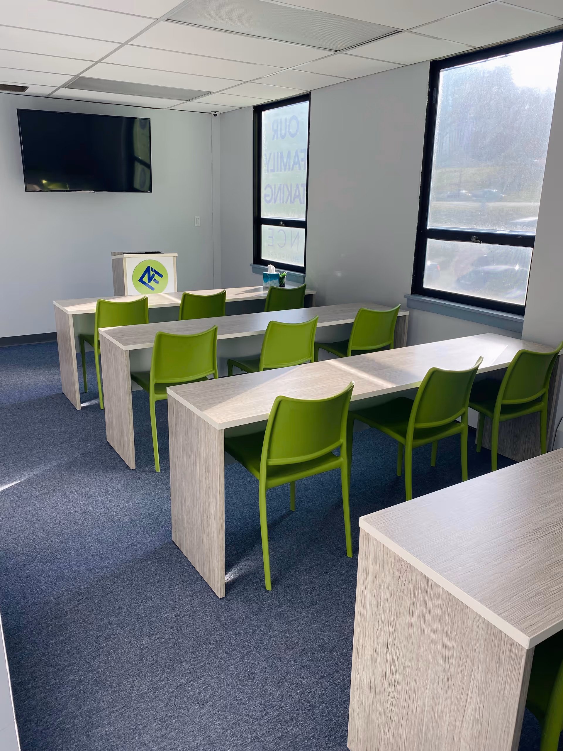 Bright training room with light wood desks, lime green chairs, a wall TV, and large windows.