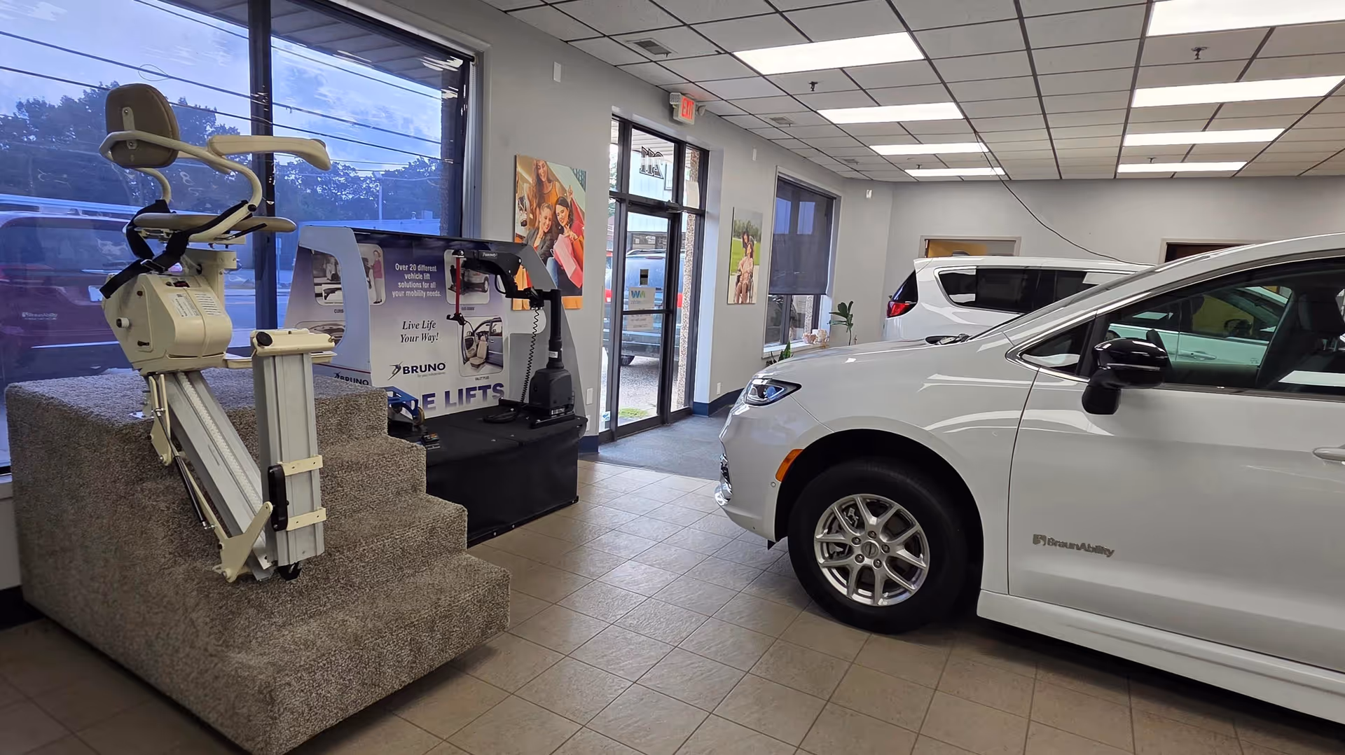 Inside a MobilityWorks showroom, a white car is displayed beside lift equipment and posters.