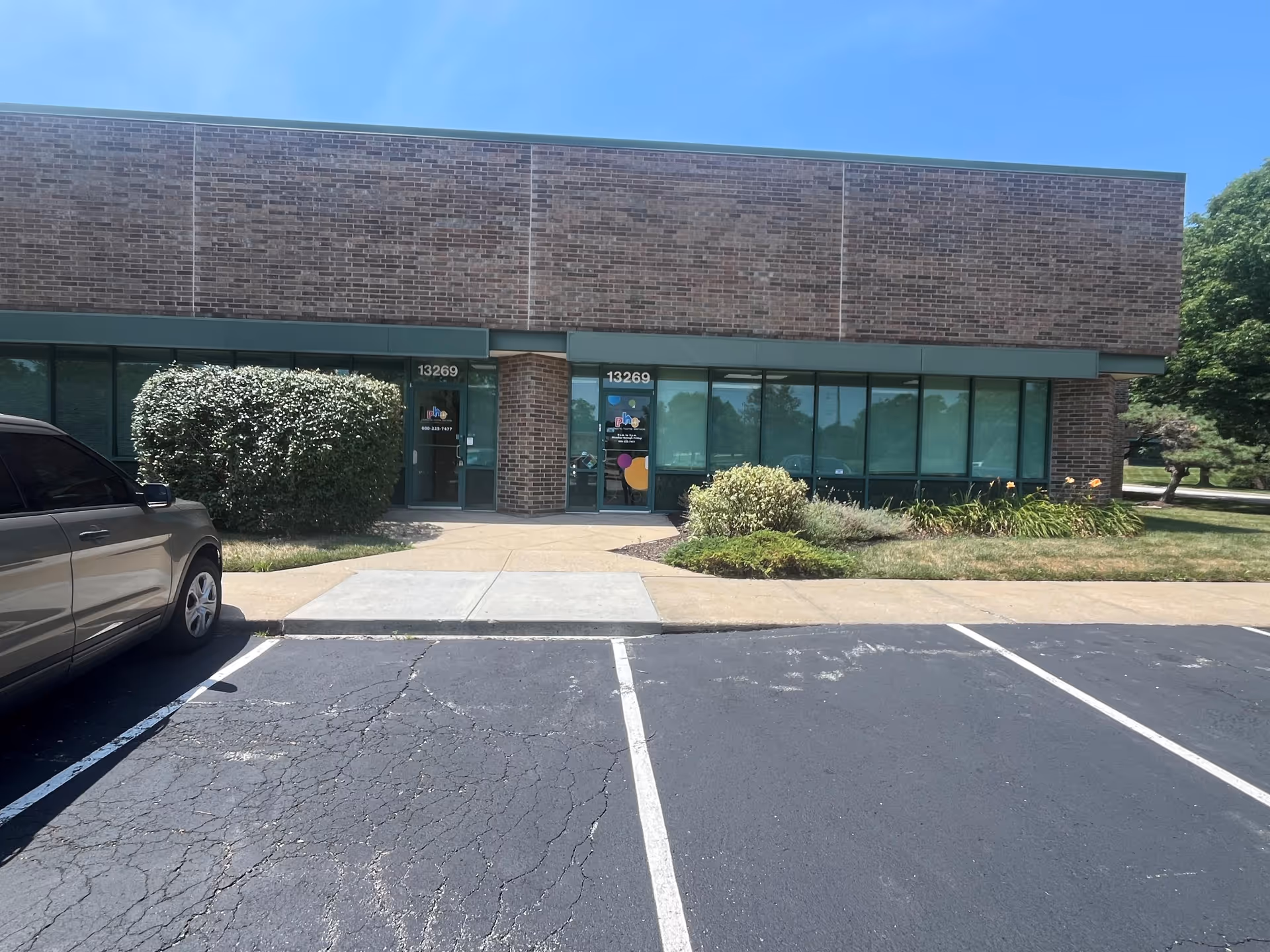 Brick, single-story storefront with glass windows and two entrance doors, parking lot in front.