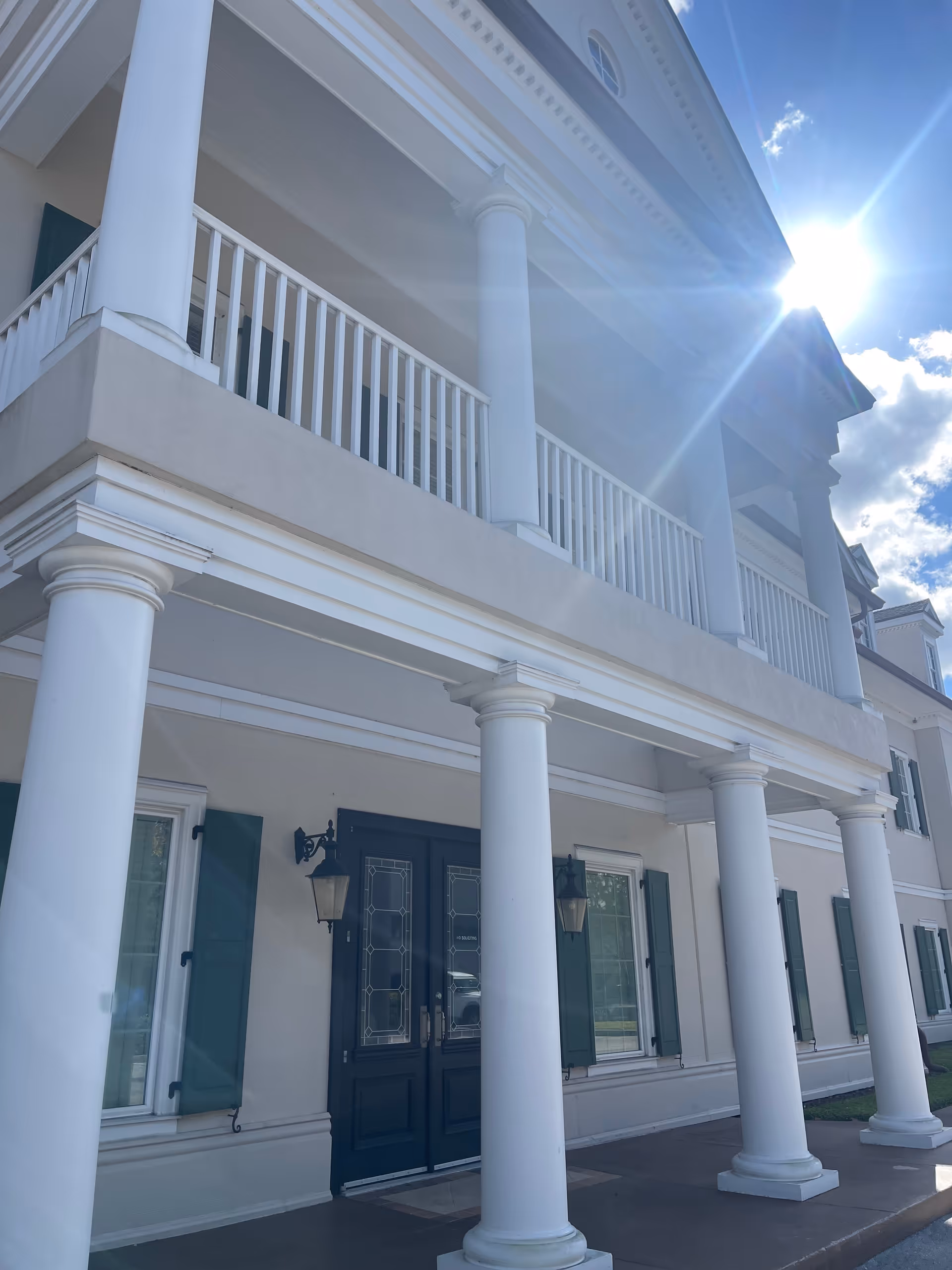 Sunny exterior view of a white, columned building with dark blue doors.