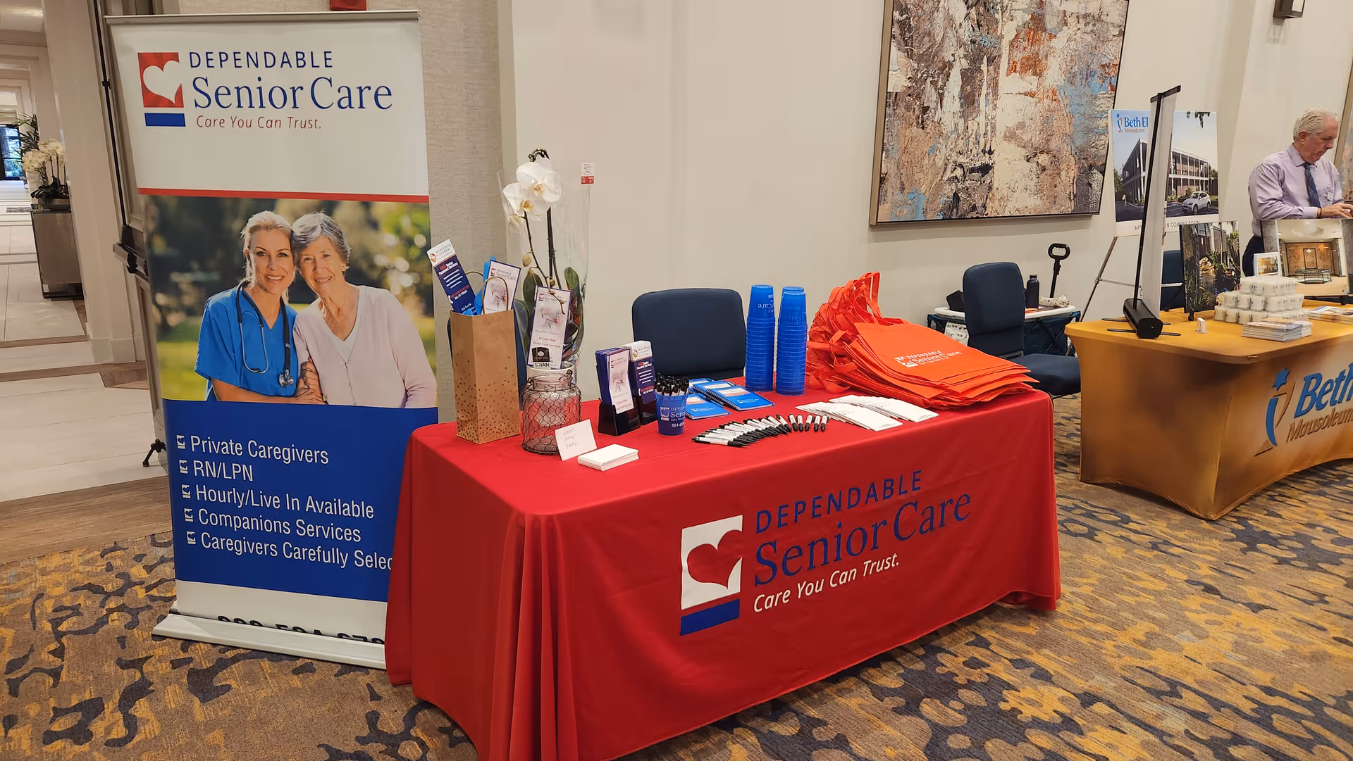 Promotional booth with Dependable Senior Care banners and a red table in an indoor lobby.