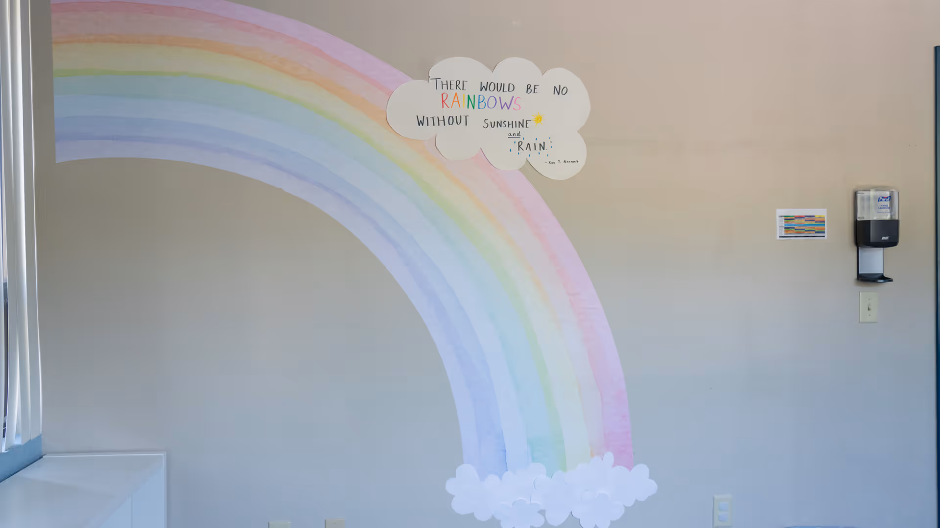 Interior wall featuring a large rainbow mural with clouds and a wall-mounted dispenser.