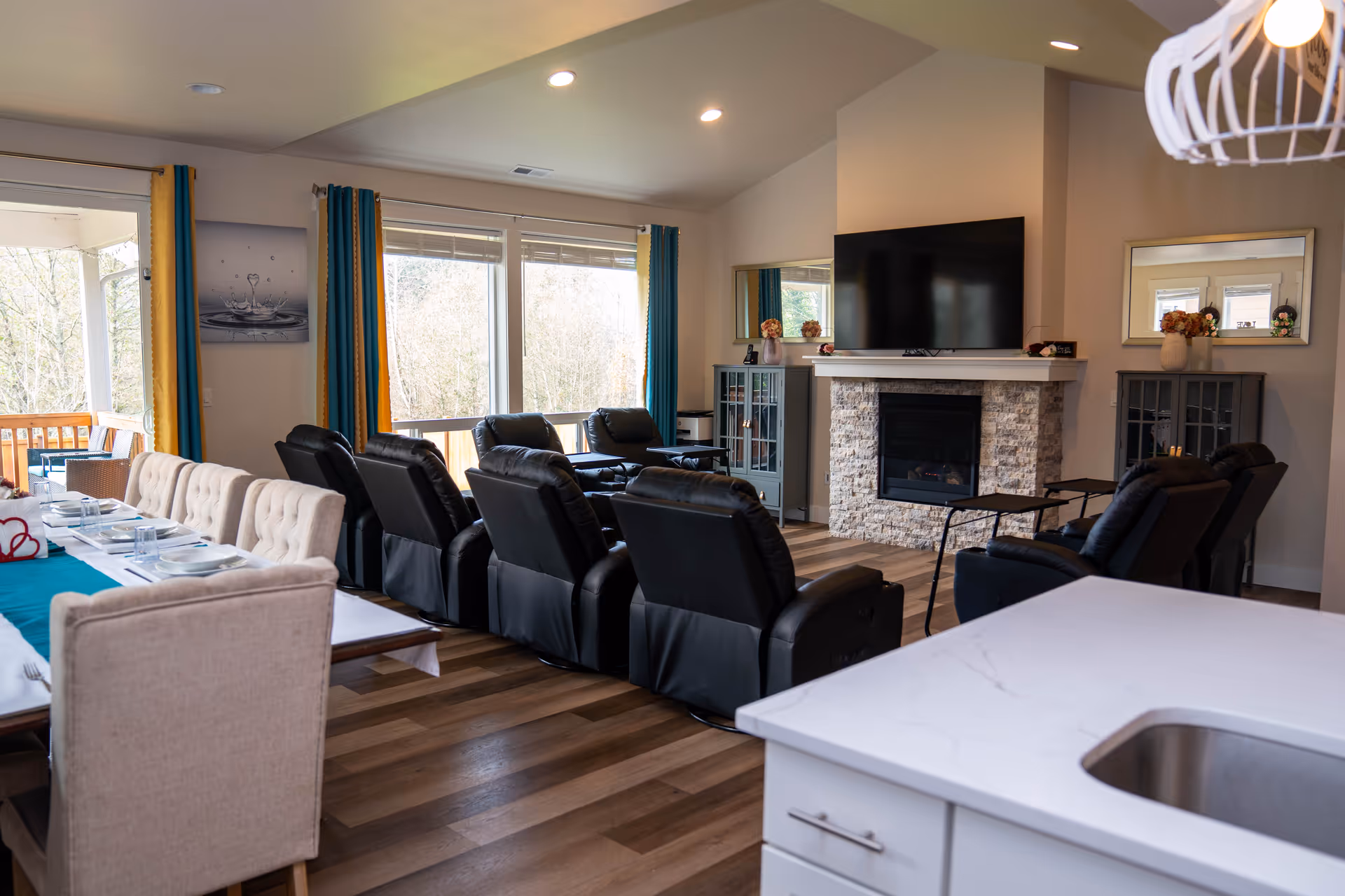 Bright living room with black recliners, dining table, and a stone fireplace with a mounted TV.