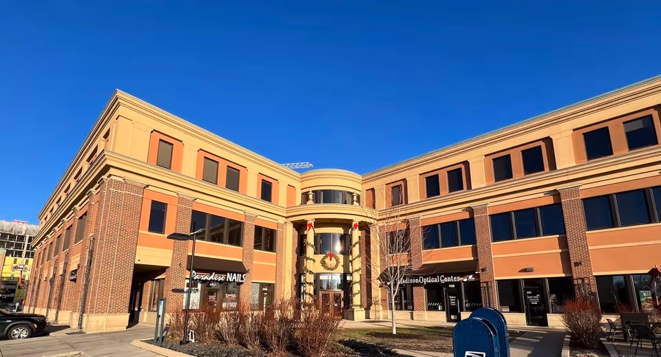 Exterior view of a multi-tenant brick building with storefronts and a clear blue sky.