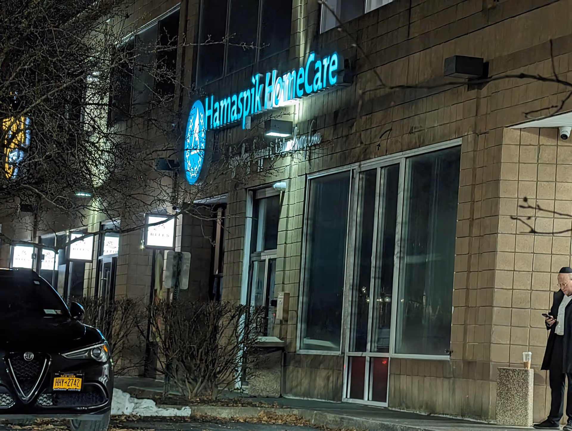 Night exterior of Hamaspik HomeCare building with turquoise sign, parked car, and a man outside.