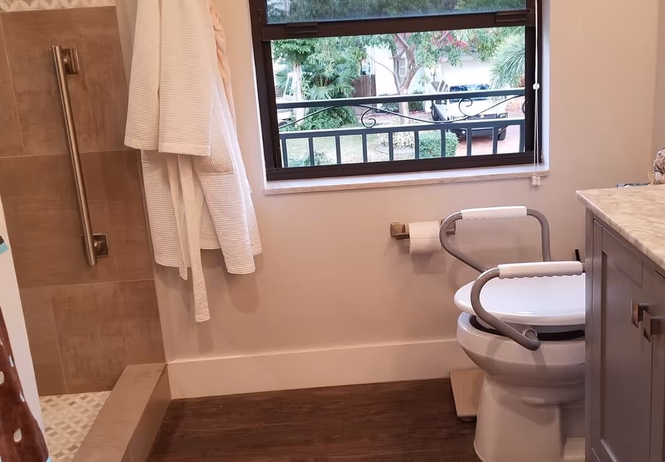 Bright bathroom with grab bars, a toilet, towel, and window view.