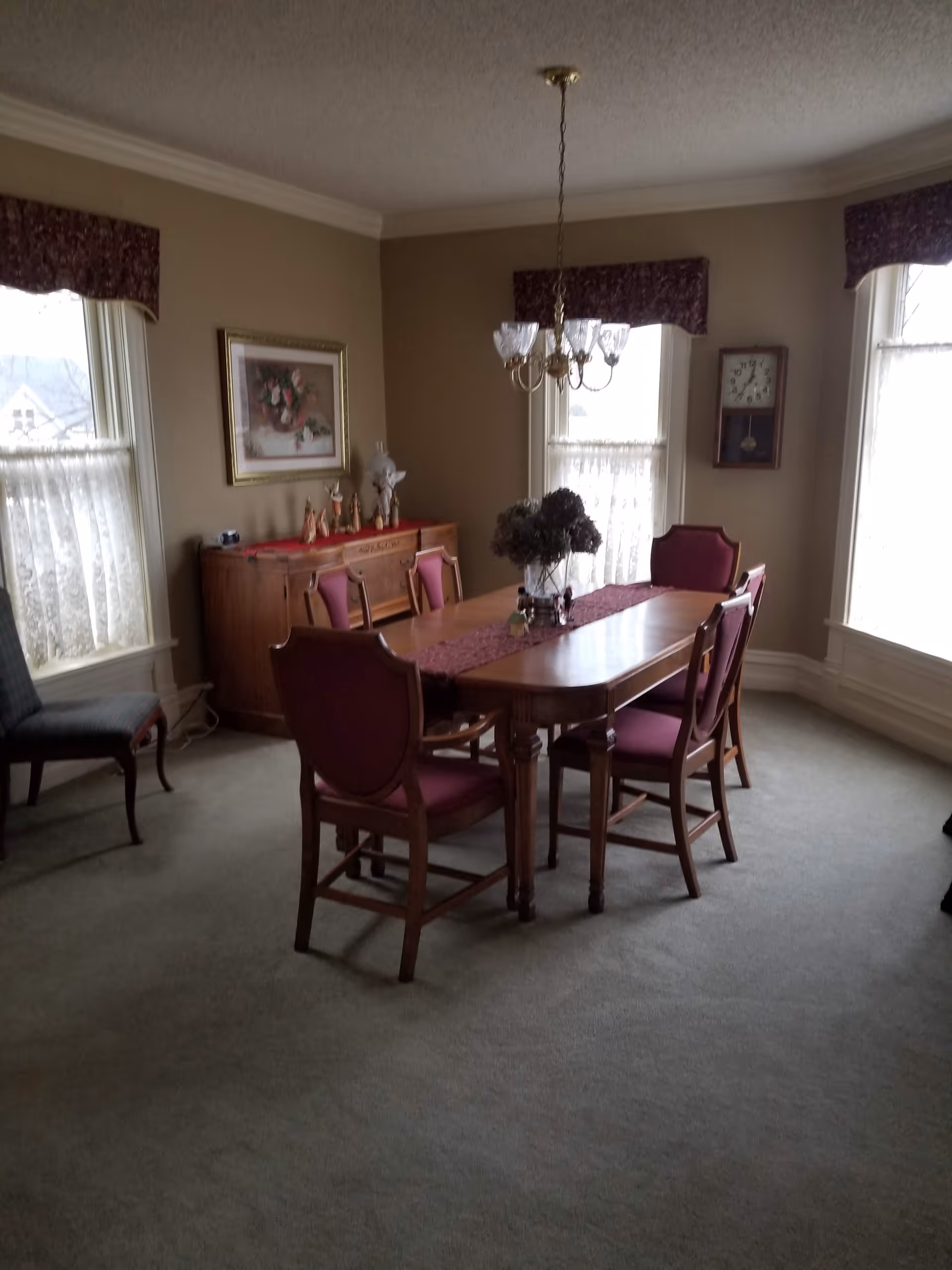 A traditional dining room with a wooden table, upholstered chairs, chandelier, and sideboard.