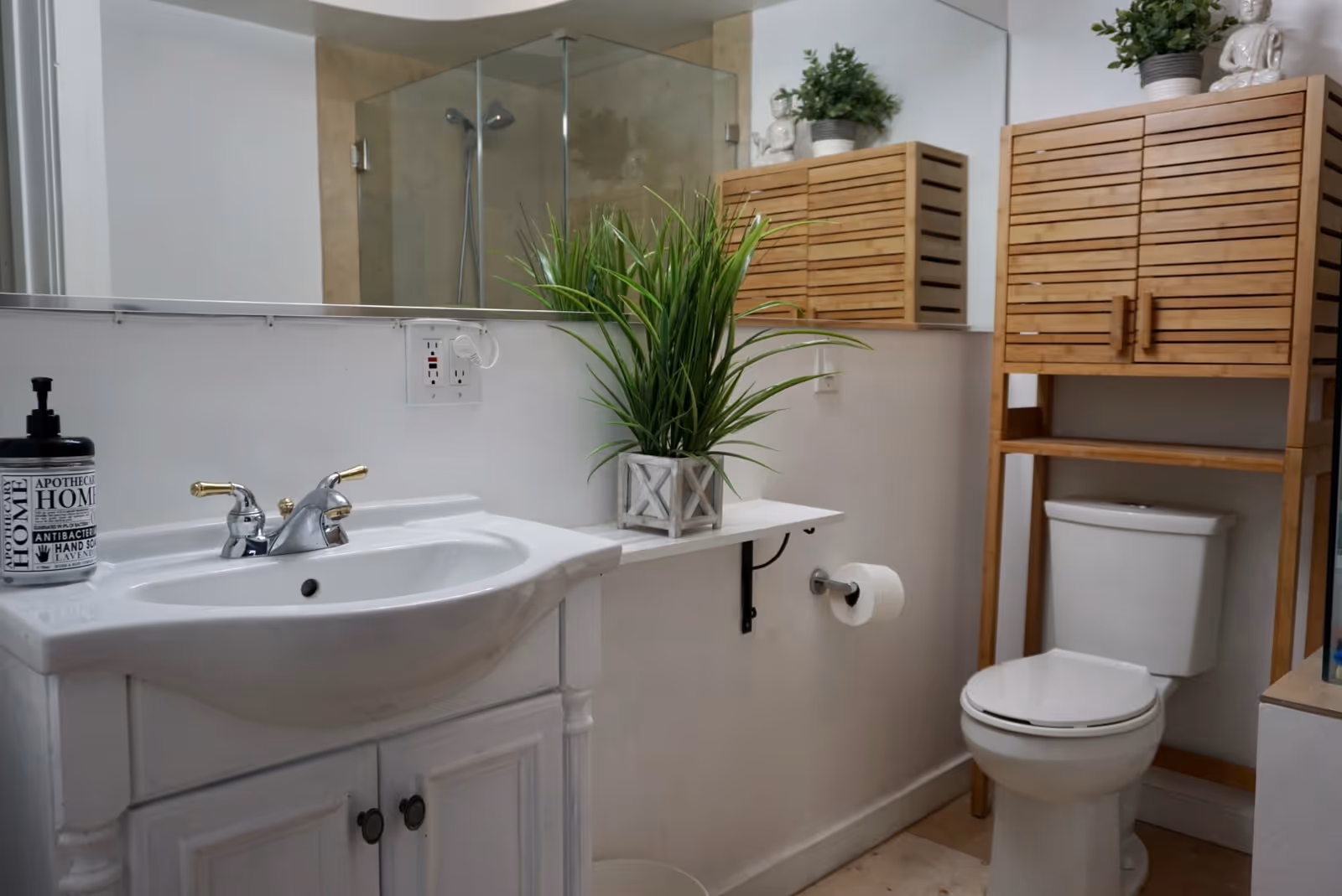A bright bathroom featuring sink, toilet, wooden storage cabinet, and potted plants.