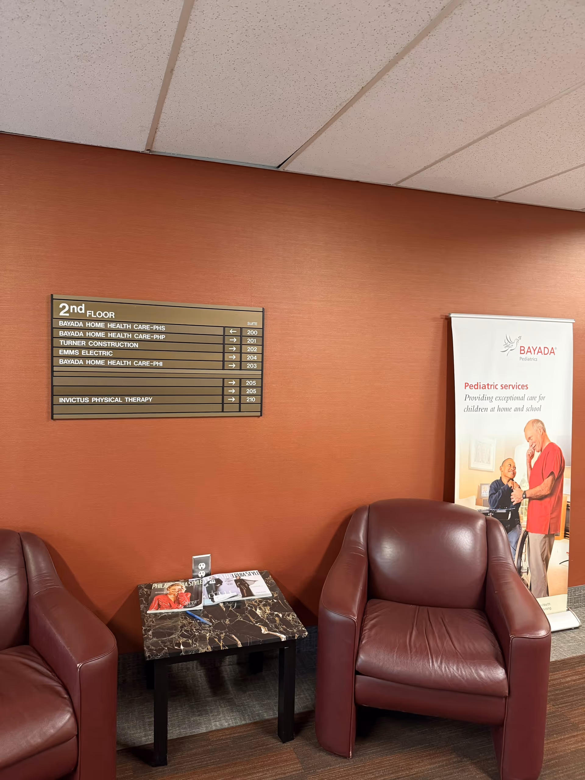 Two maroon chairs and a marble-topped table sit in a red-walled lobby with directory sign.