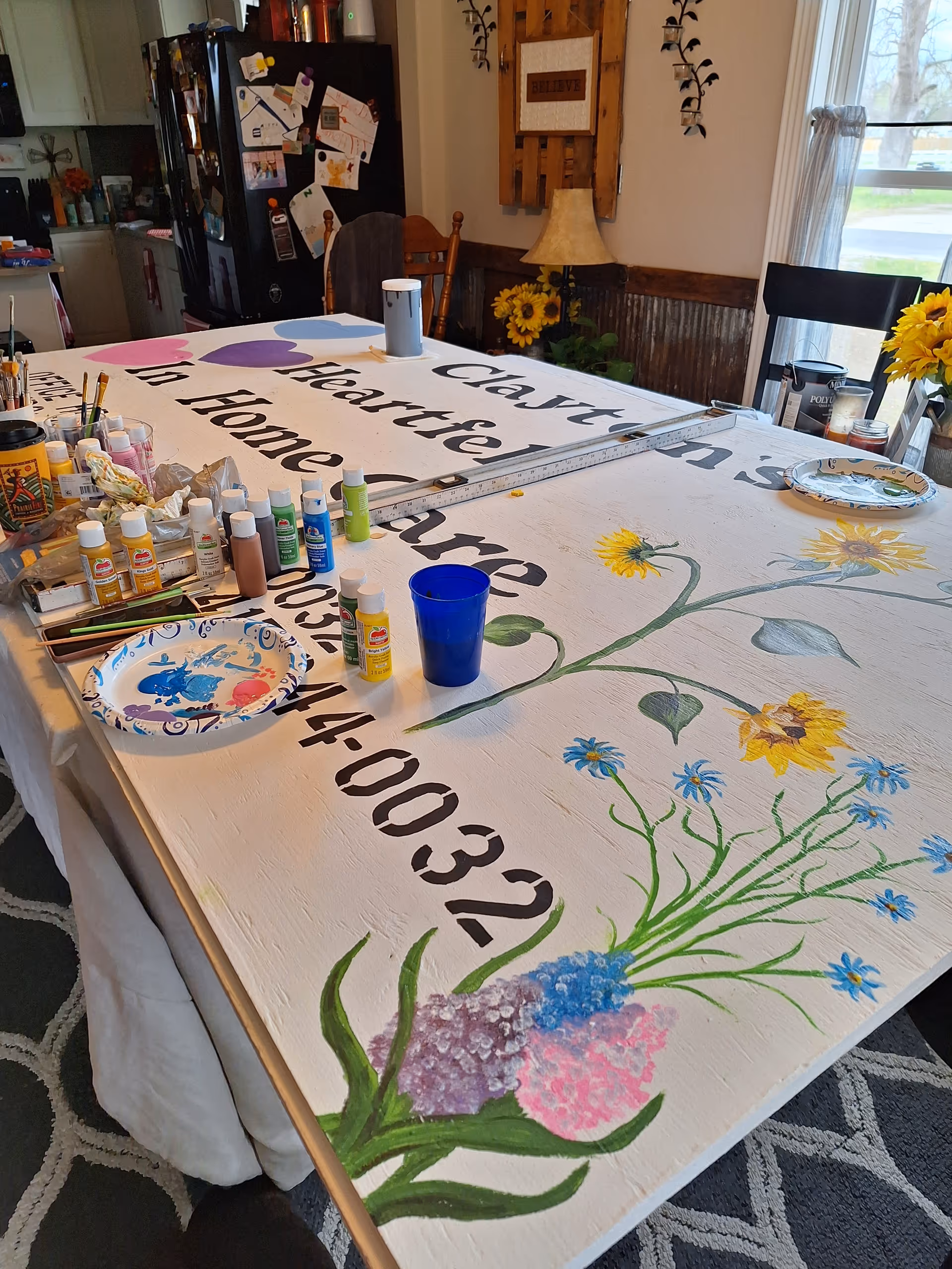 A large table covered with art supplies and a painted banner for Clayton's Heartfelt Home Care.