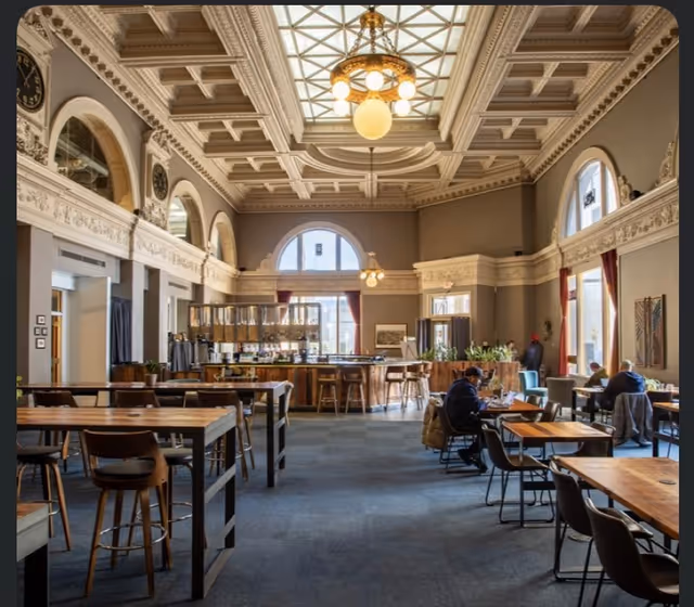 Elegant dining hall with high ornate ceiling, chandeliers, and residents seated at tables.