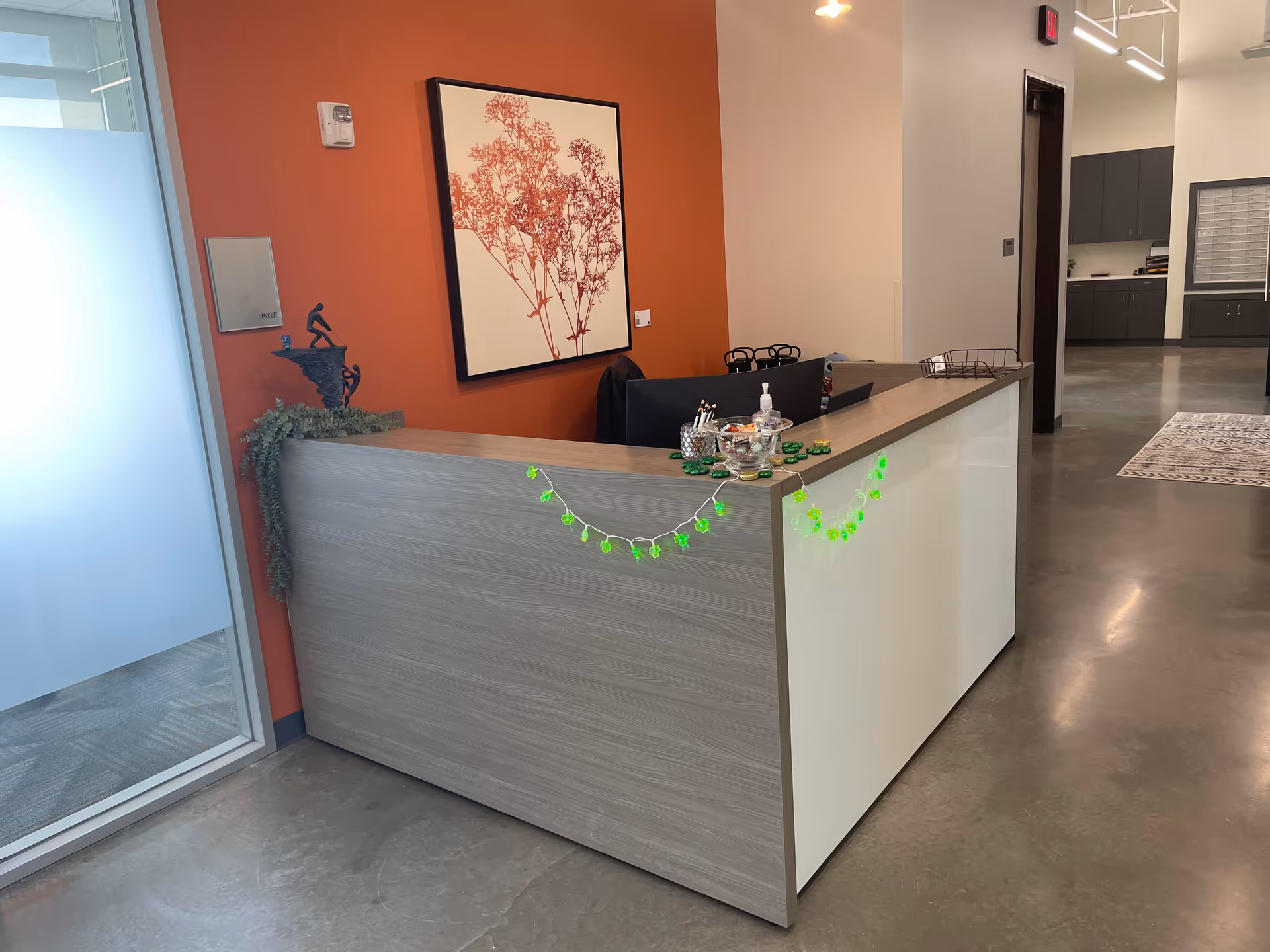 Modern reception desk in an orange-walled lobby with plants and green garland.