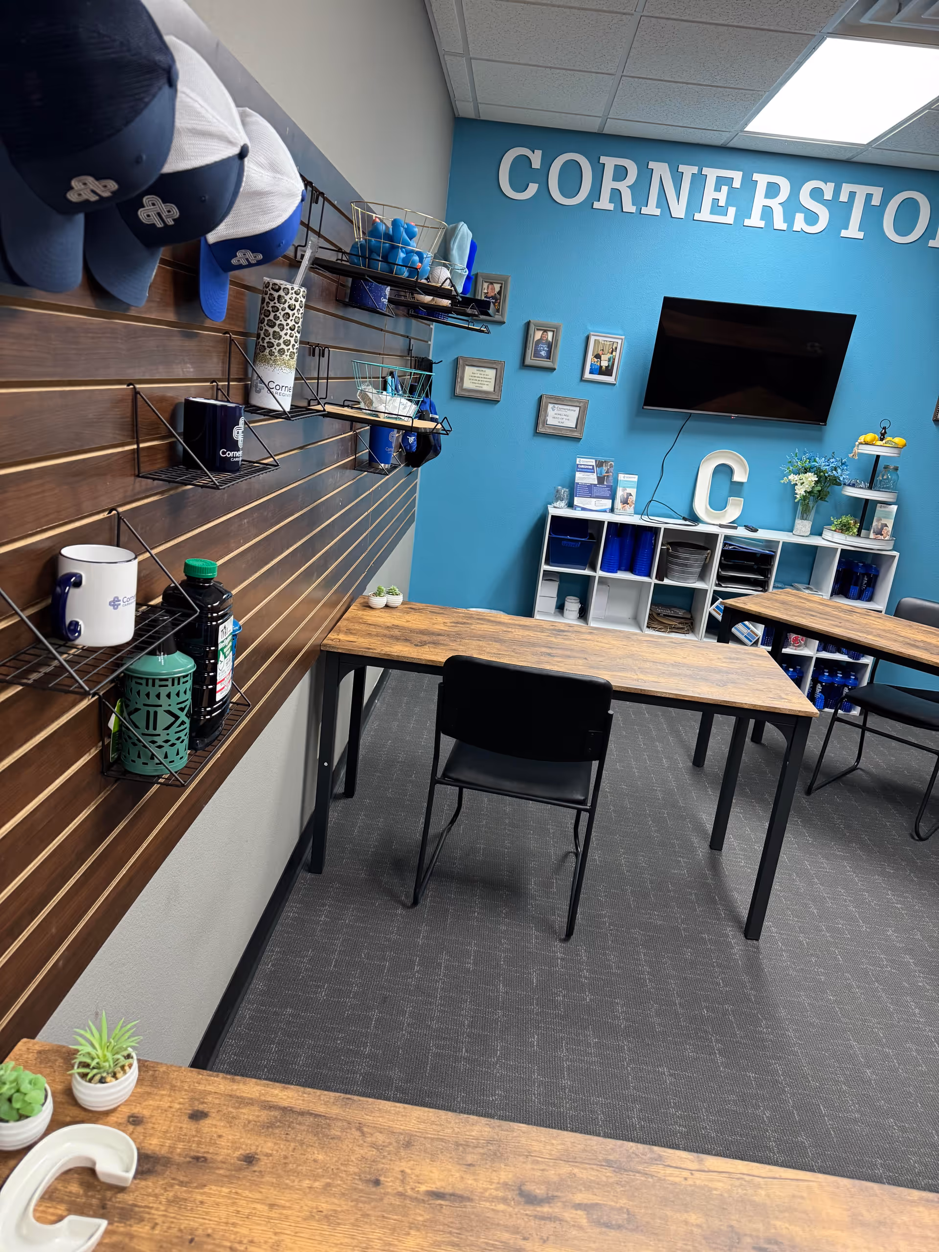 Indoor activity room with wooden tables, blue wall, shelves, and Cornerstone Caregiving branding.