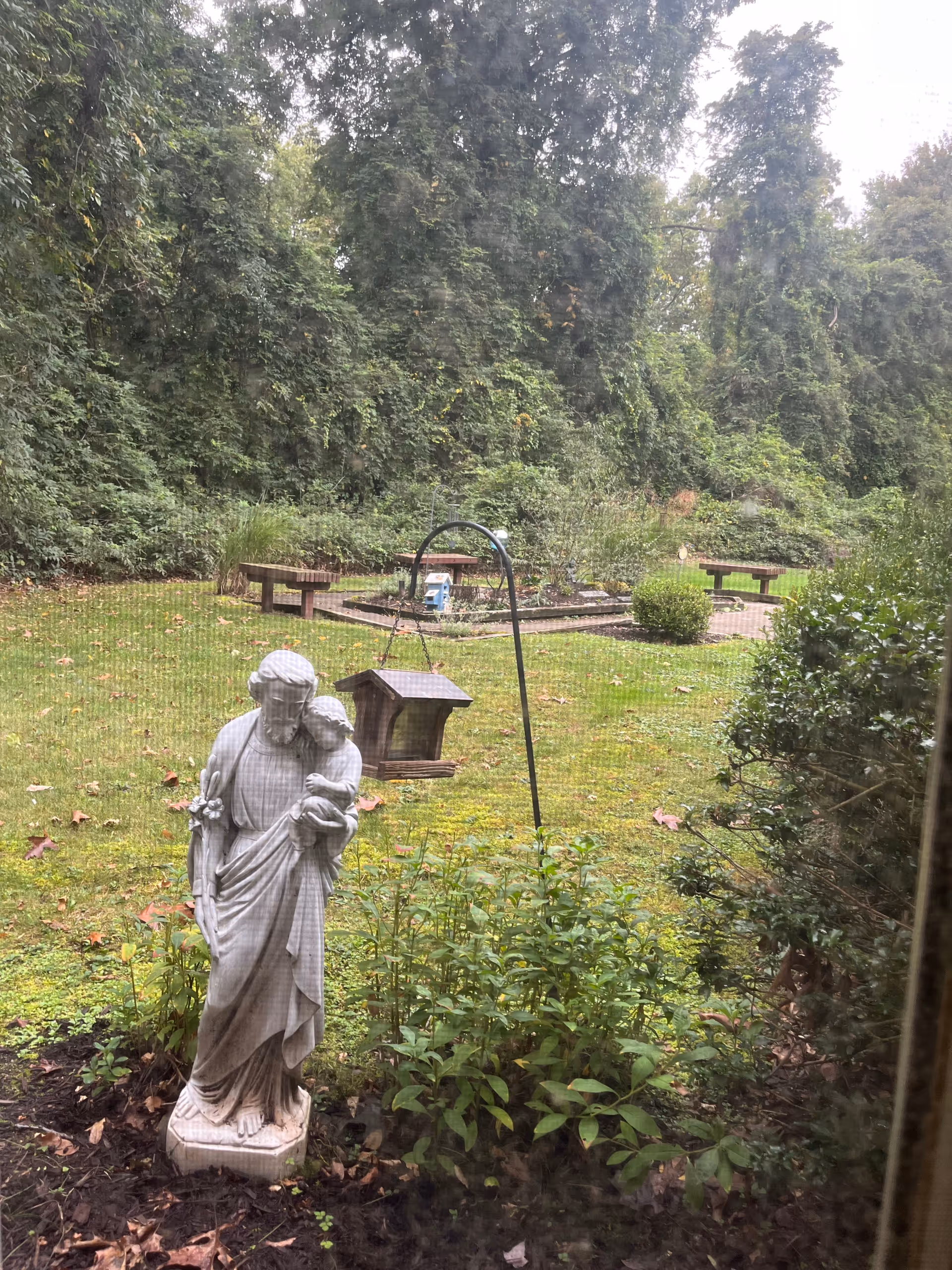 Outdoor garden scene with a statue, bird feeder, and benches.