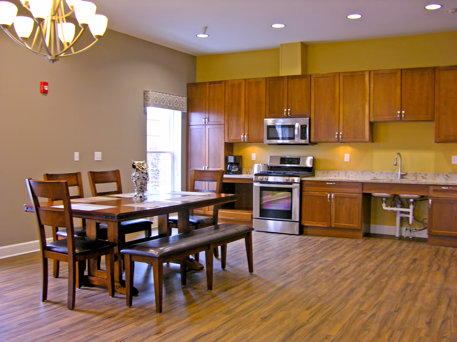 A spacious kitchen with wooden cabinets, stainless stove, and a dining table in a bright room.