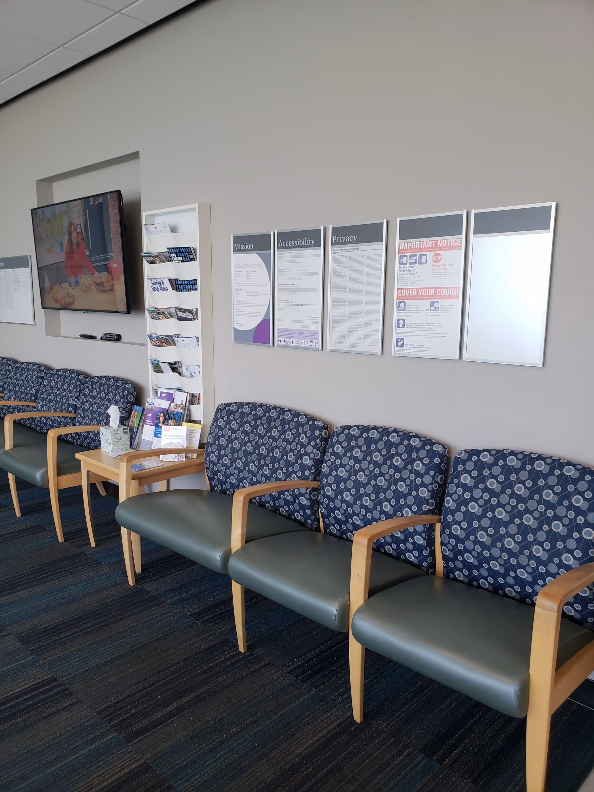 Row of blue patterned chairs along a wall with brochures and a TV.