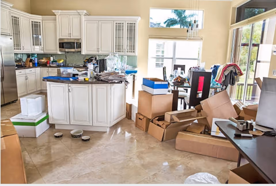 Open kitchen with white cabinets, island, and cluttered boxes across the floor.
