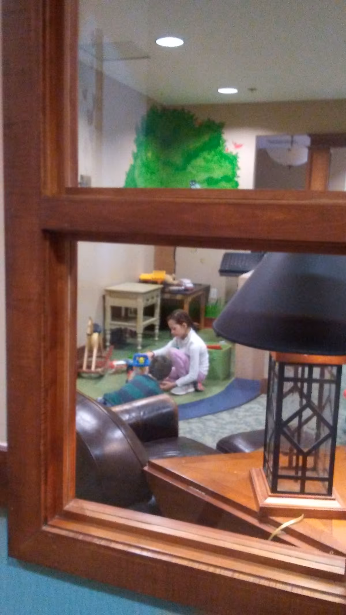 Two people play with toys on a mat in a bright indoor activity room.