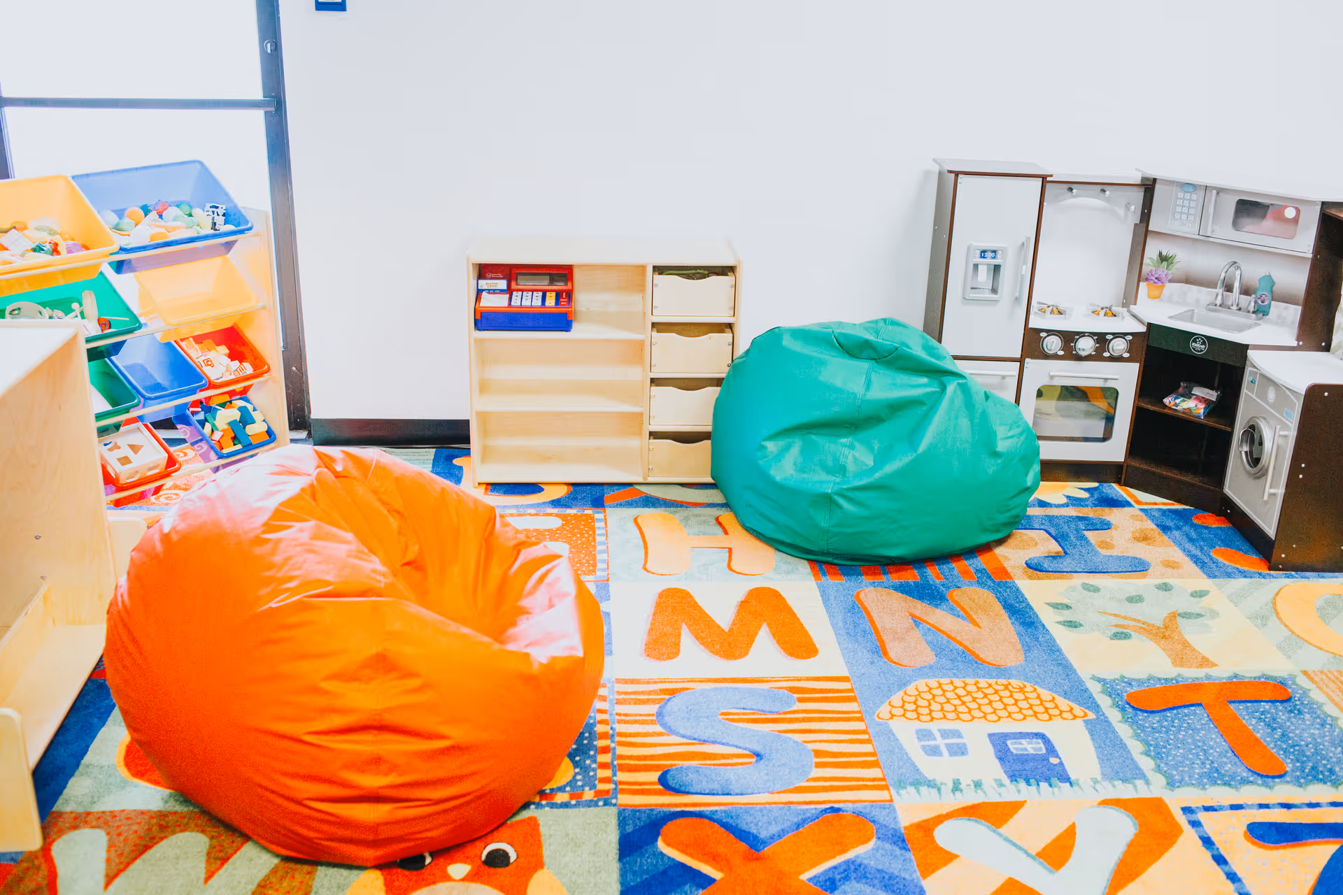 Colorful children's play area with bean bags, toy kitchen, and cubbies in a bright room.