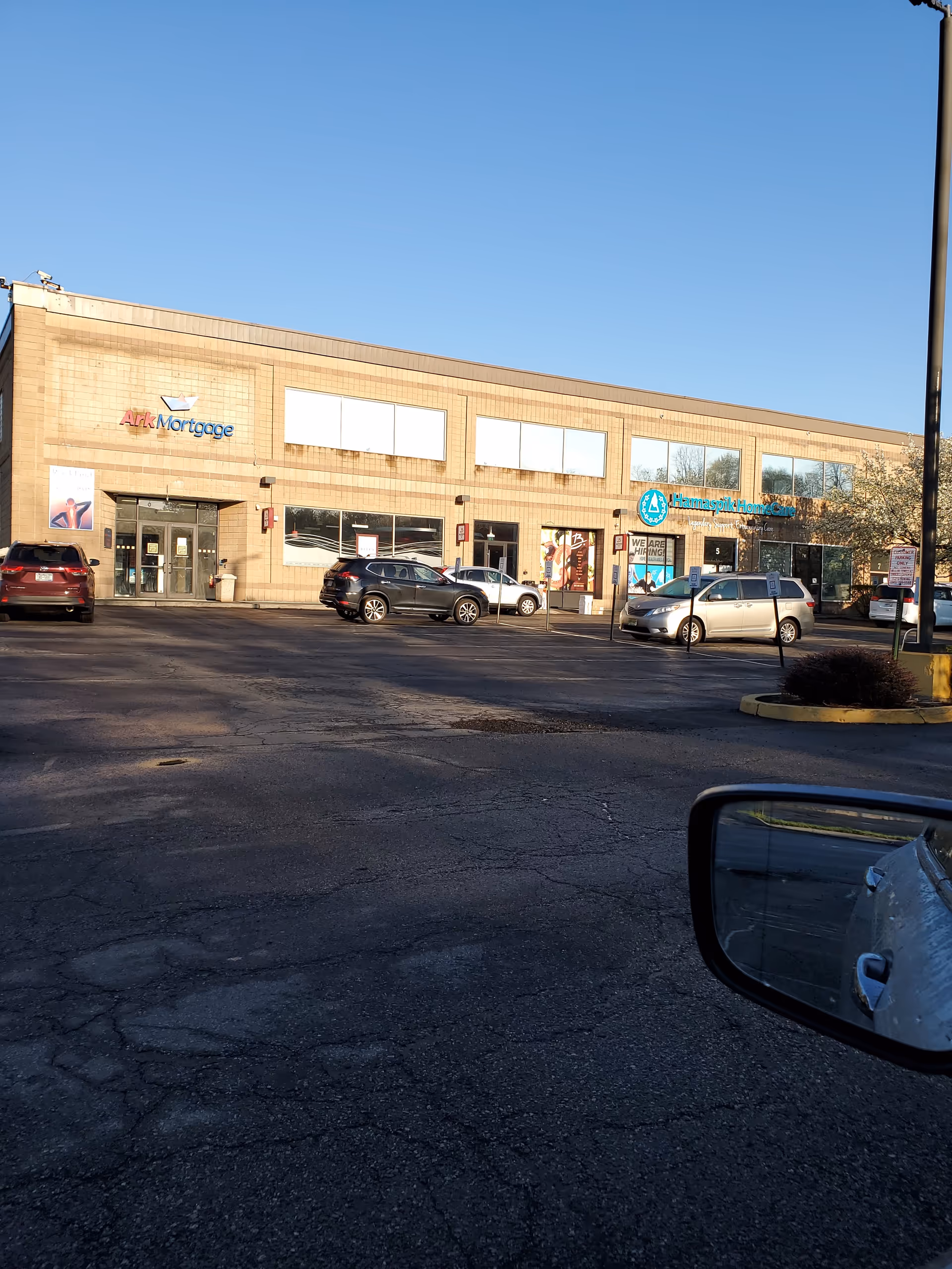 A brick retail strip with Hamaspik HomeCare sign and several parked cars in front.