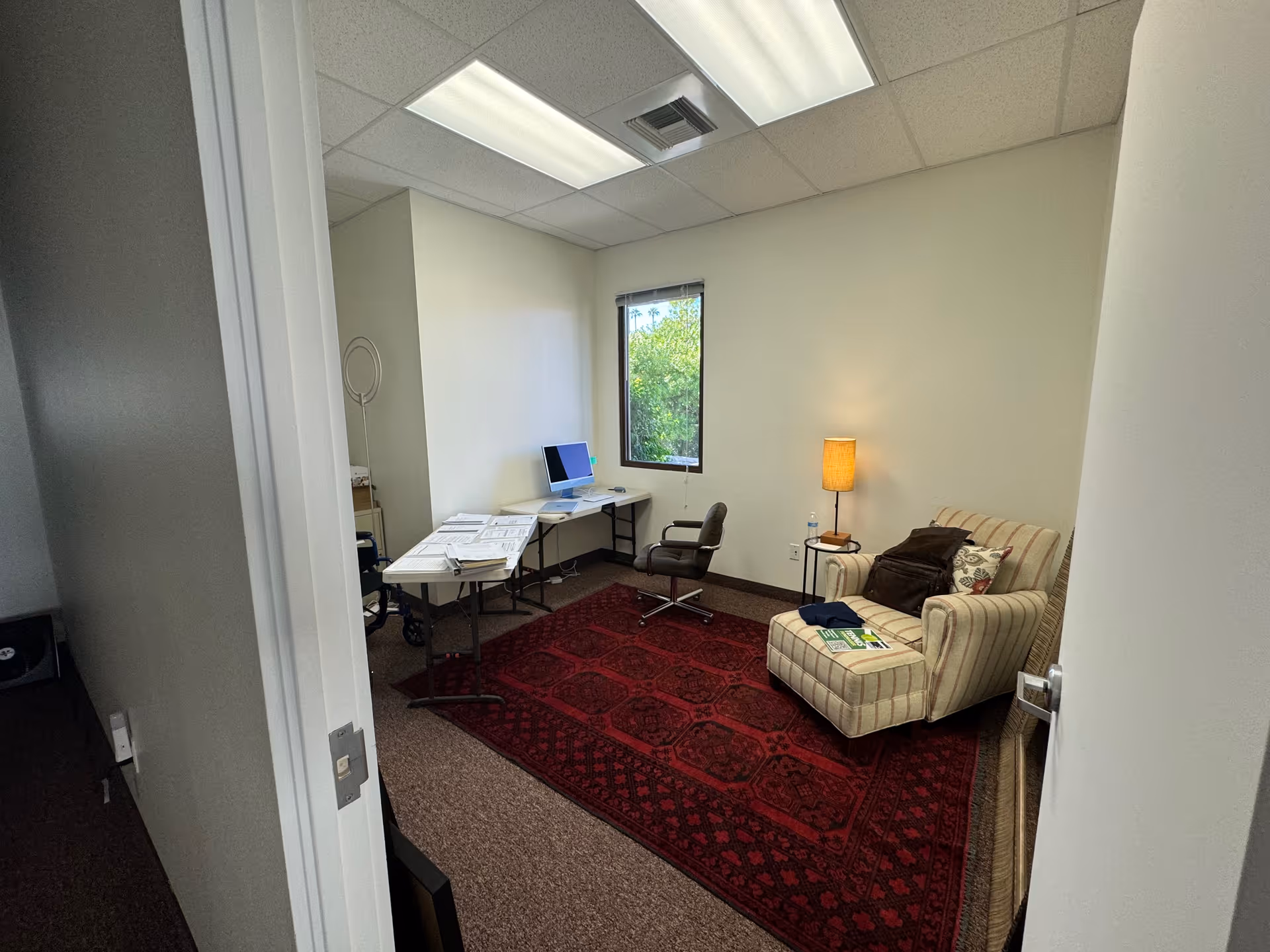 Small staff office in a senior facility featuring a desk, computer, window, and armchair seating.