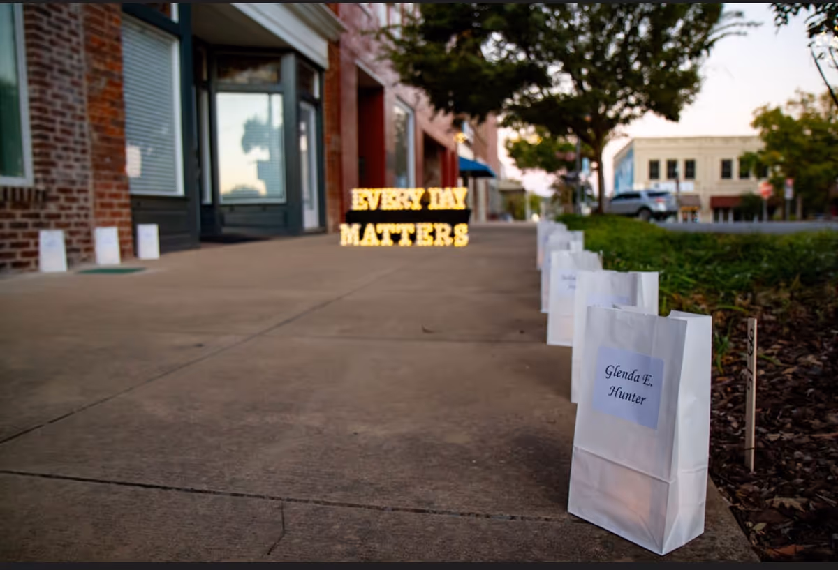 Outdoor sidewalk scene with white gift bags along the path and a lit 'Every Day Matters' sign.