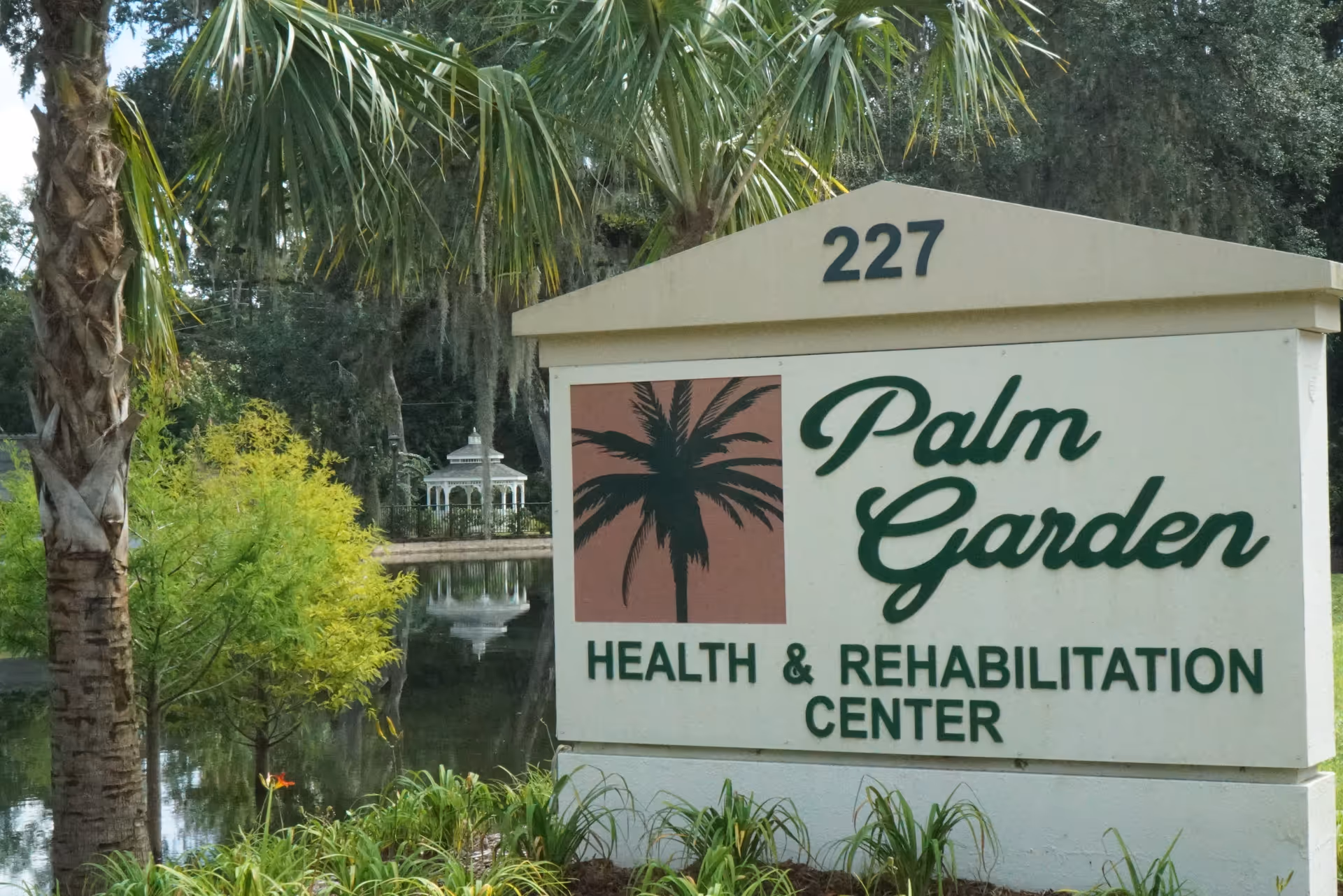 Exterior sign reads Palm Garden Health & Rehabilitation Center with palm tree logo beside water.