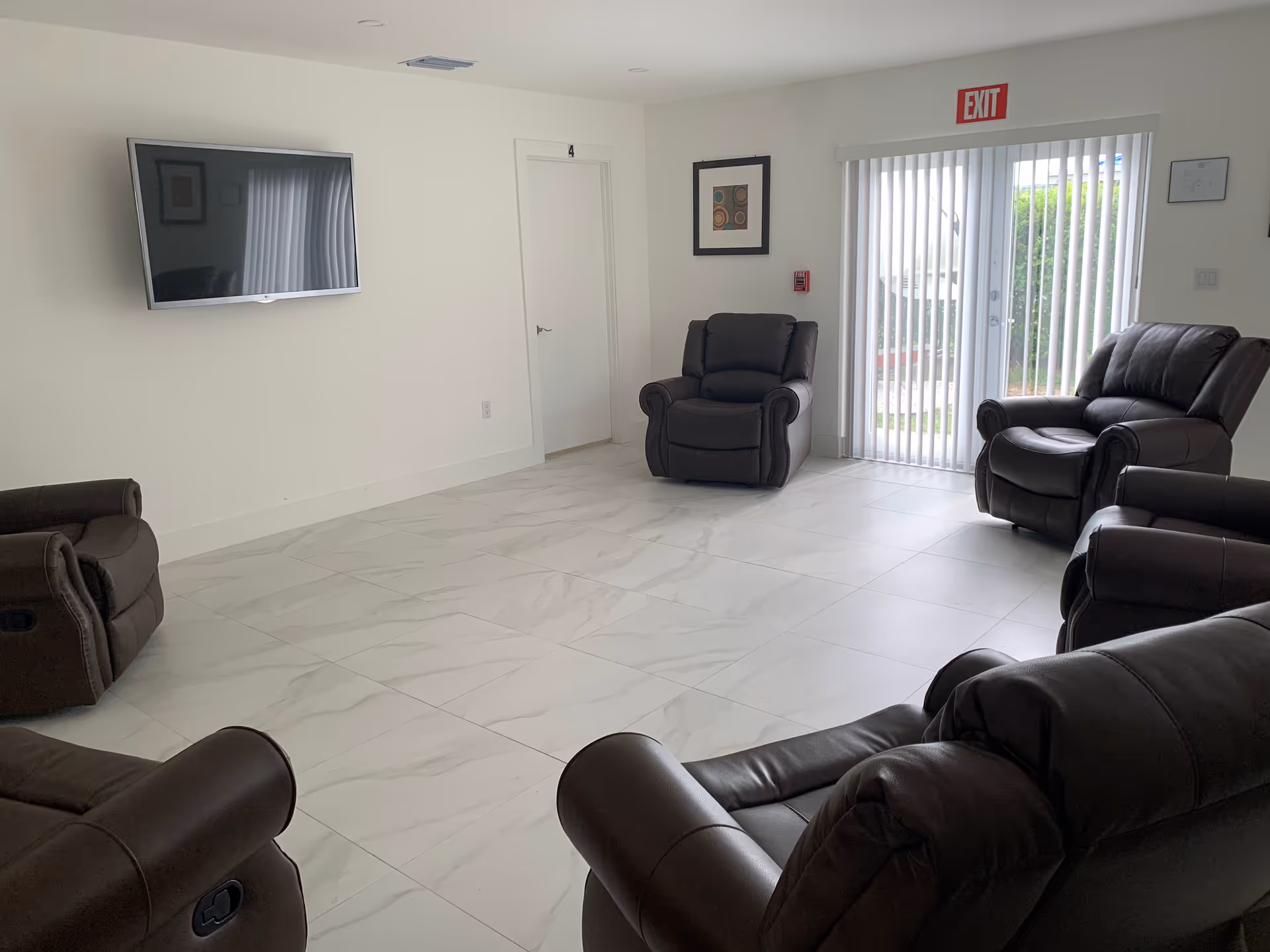 A modern senior living common lounge with dark leather recliners, TV, and sliding doors.