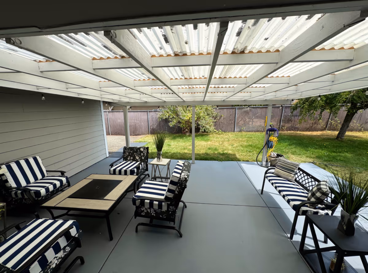 Covered outdoor patio with striped cushioned seating, coffee table, planters, and a grassy backyard beyond.