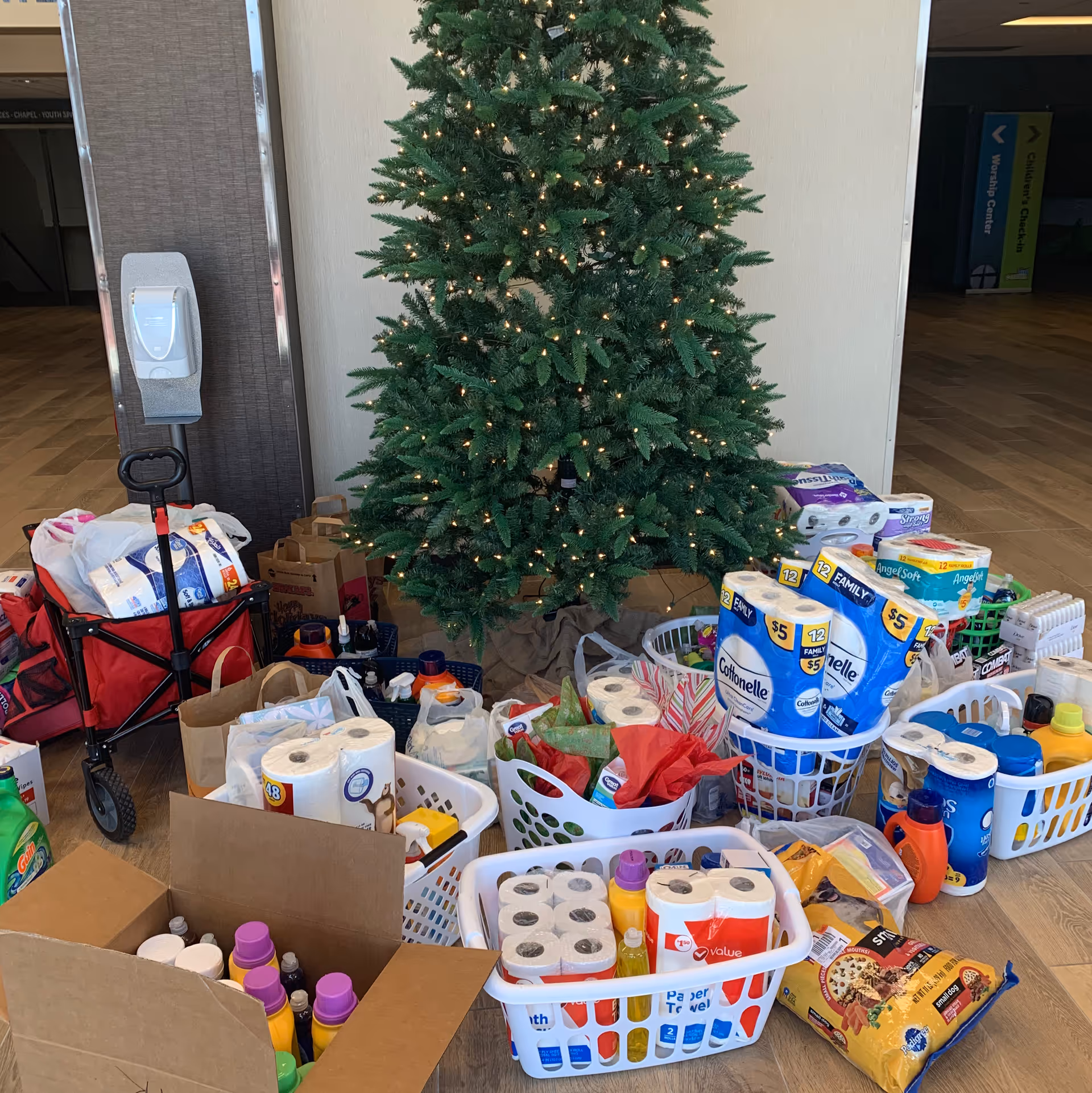 Decorated Christmas tree with baskets of donated supplies inside a senior living facility lobby.