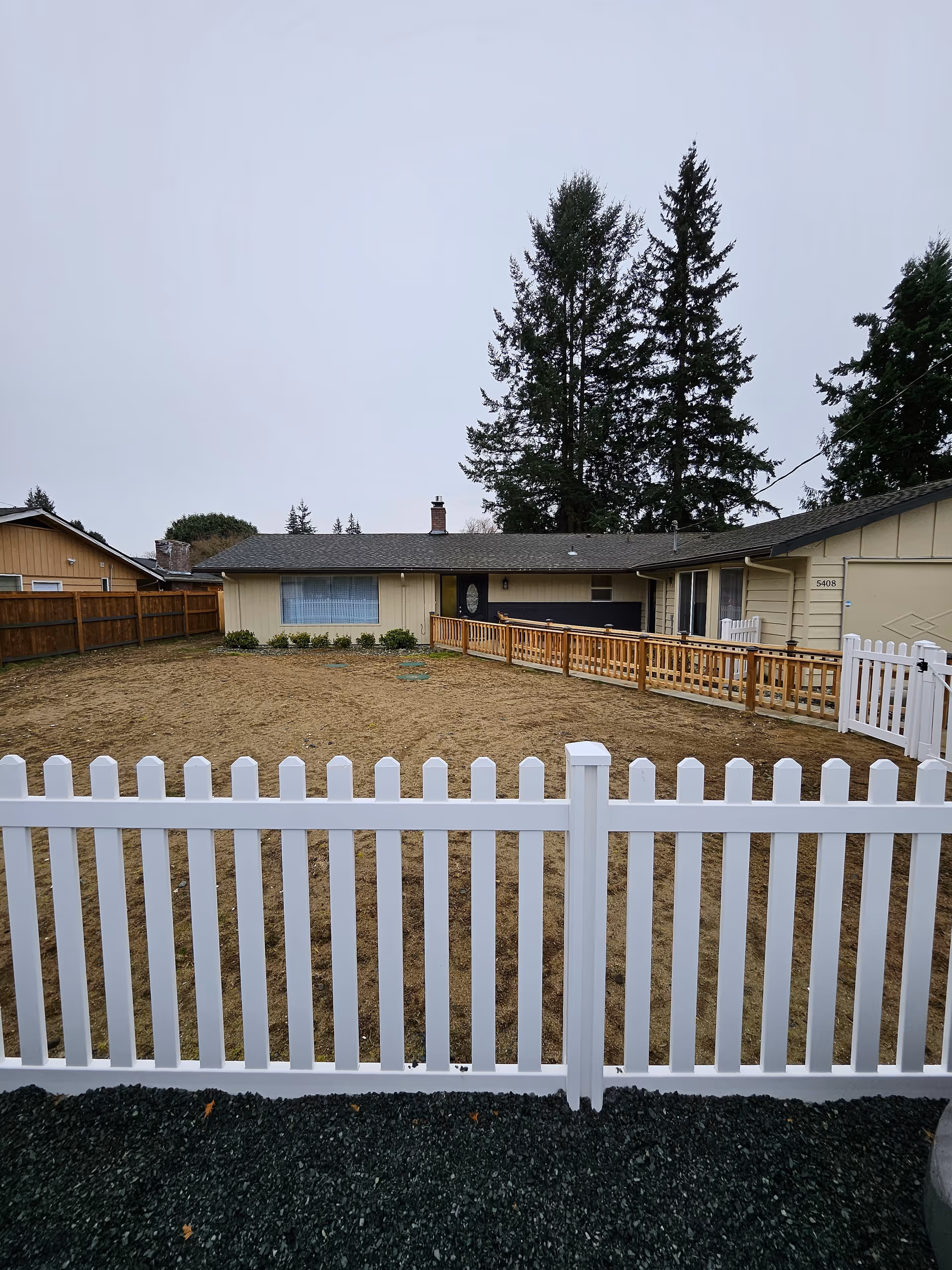 Front yard of a single-story senior home with a white picket fence and wooden ramp.