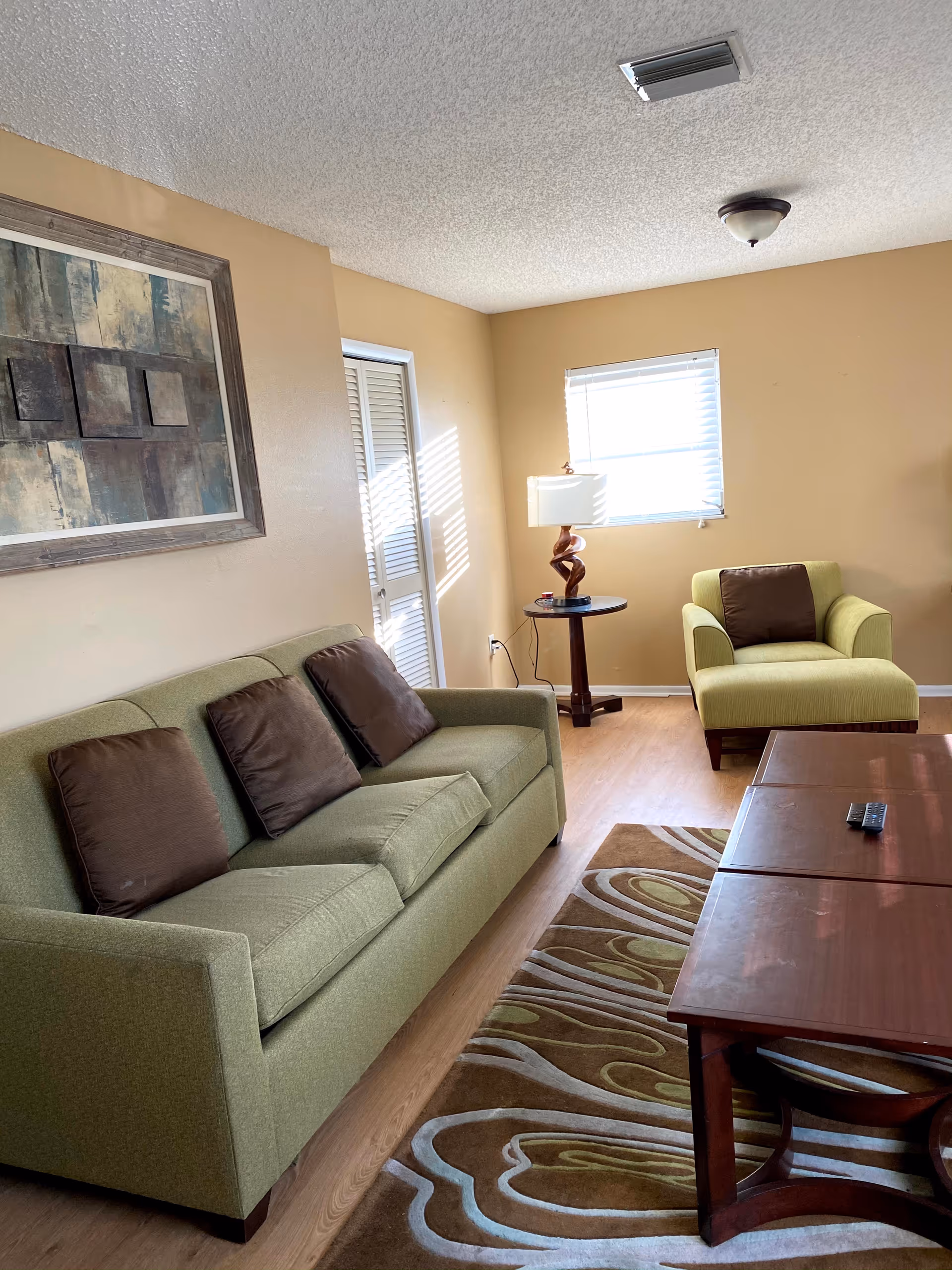 Beige living room with green sofa, chair, rug, and wooden coffee table.