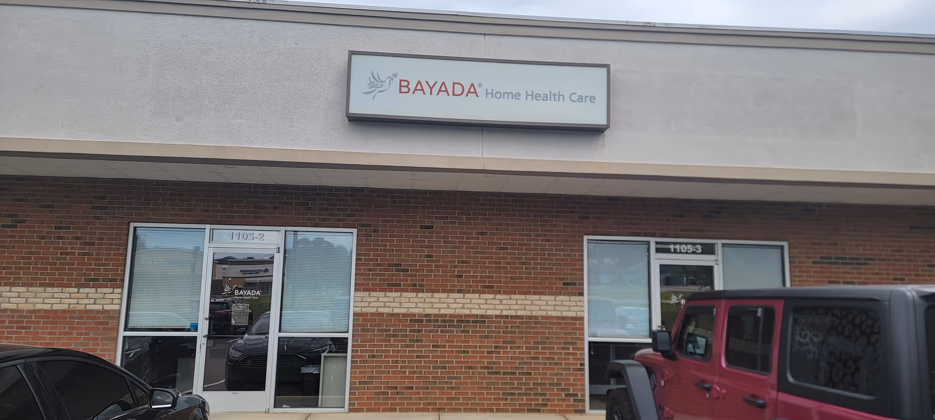 Exterior view of a BAYADA building with a sign, brick facade, and parked cars.