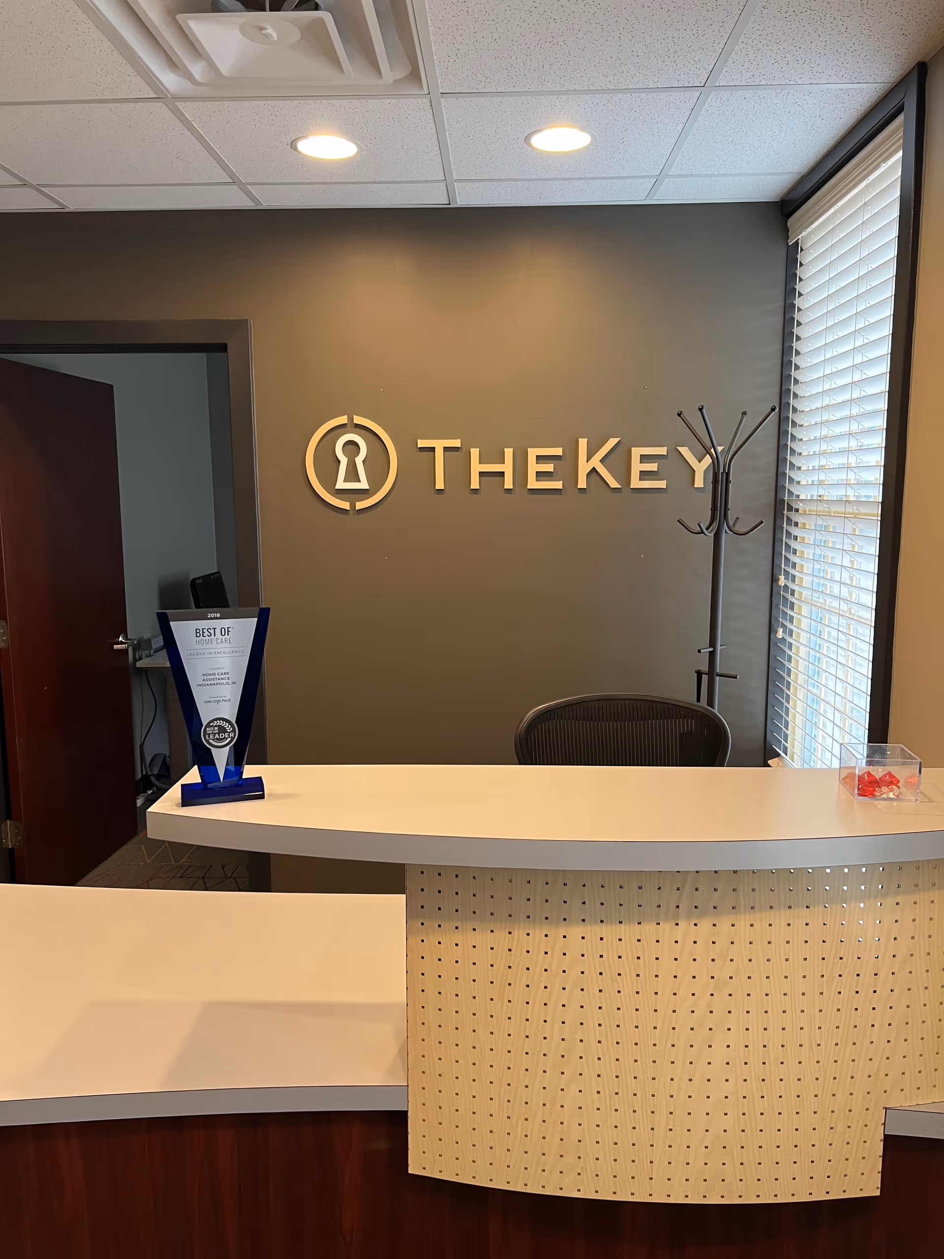 Reception desk with TheKey logo on wall and a coat rack in a modern lobby.
