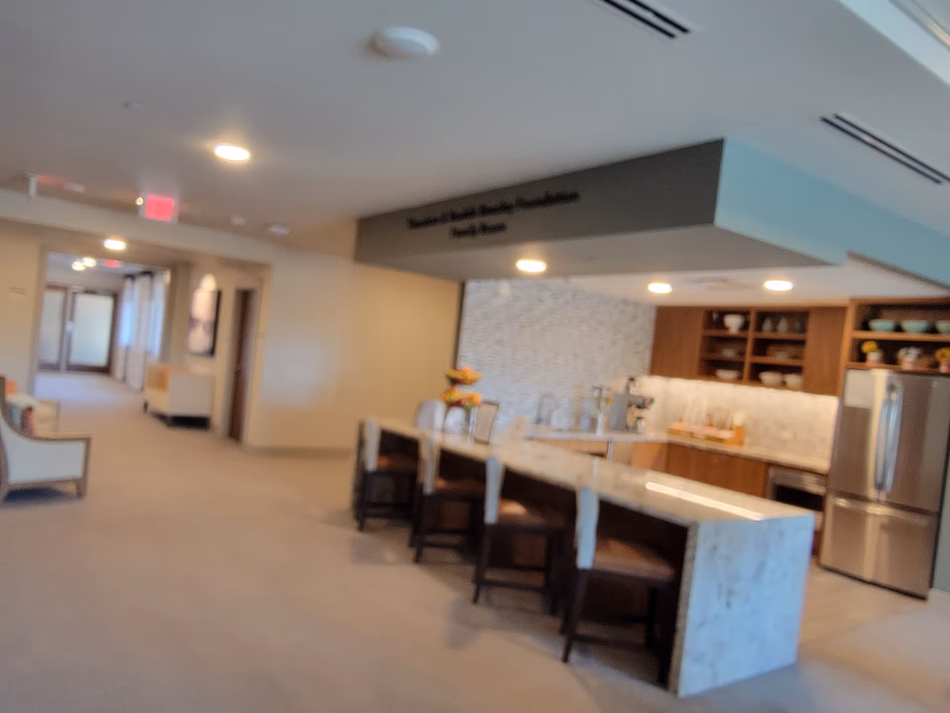 Interior common area with a kitchen island, stools, and cabinetry in a senior living facility.