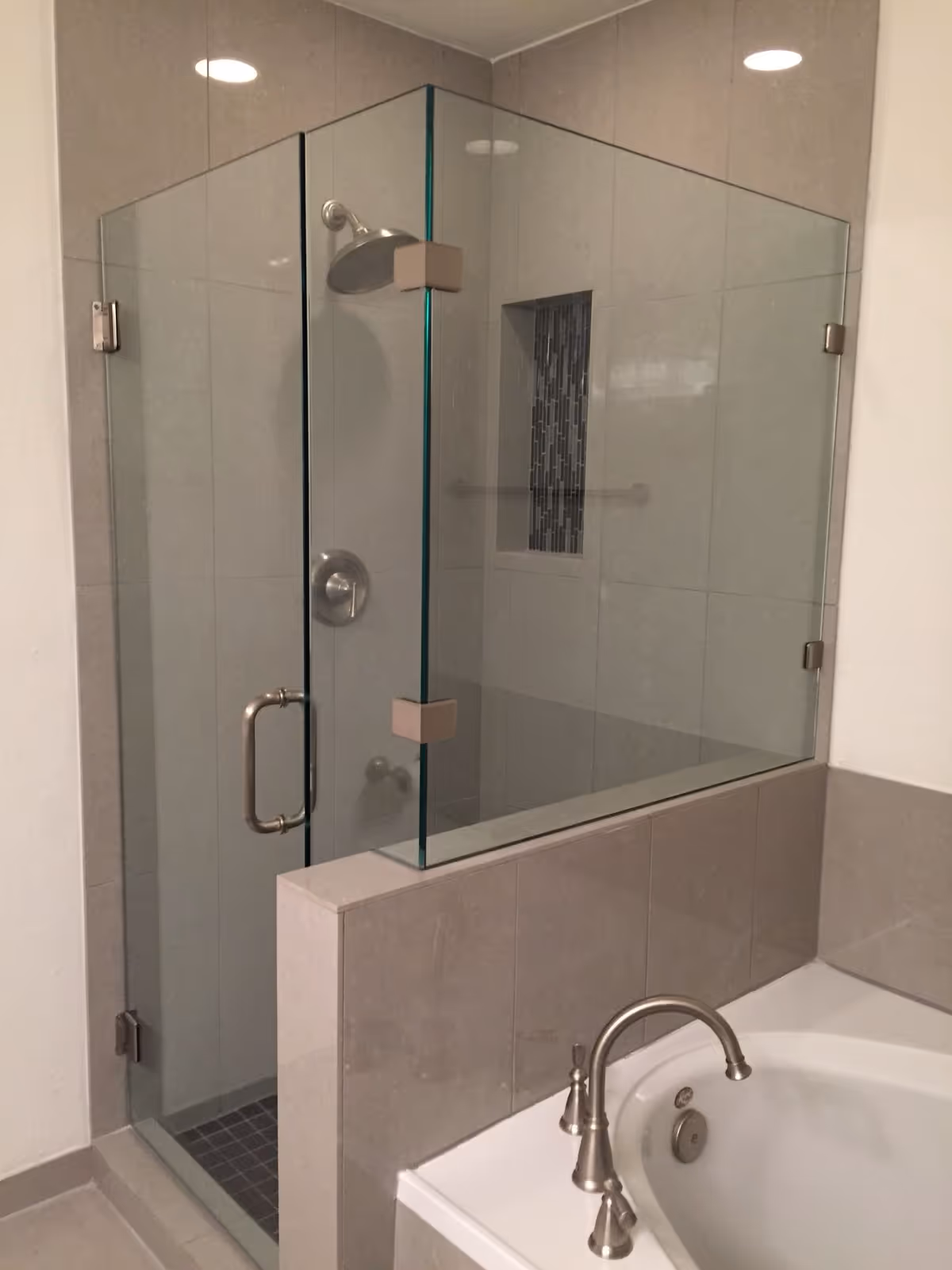 Glass-framed shower enclosure adjacent to a tiled bathtub in a modern bathroom.