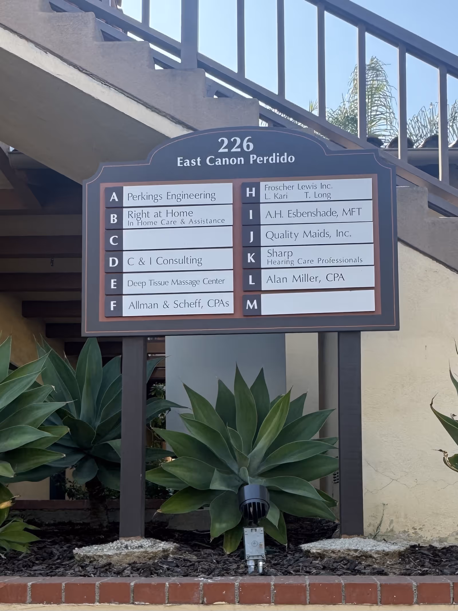 Exterior signboard for Right at Home with unit listings near stairs and plants.