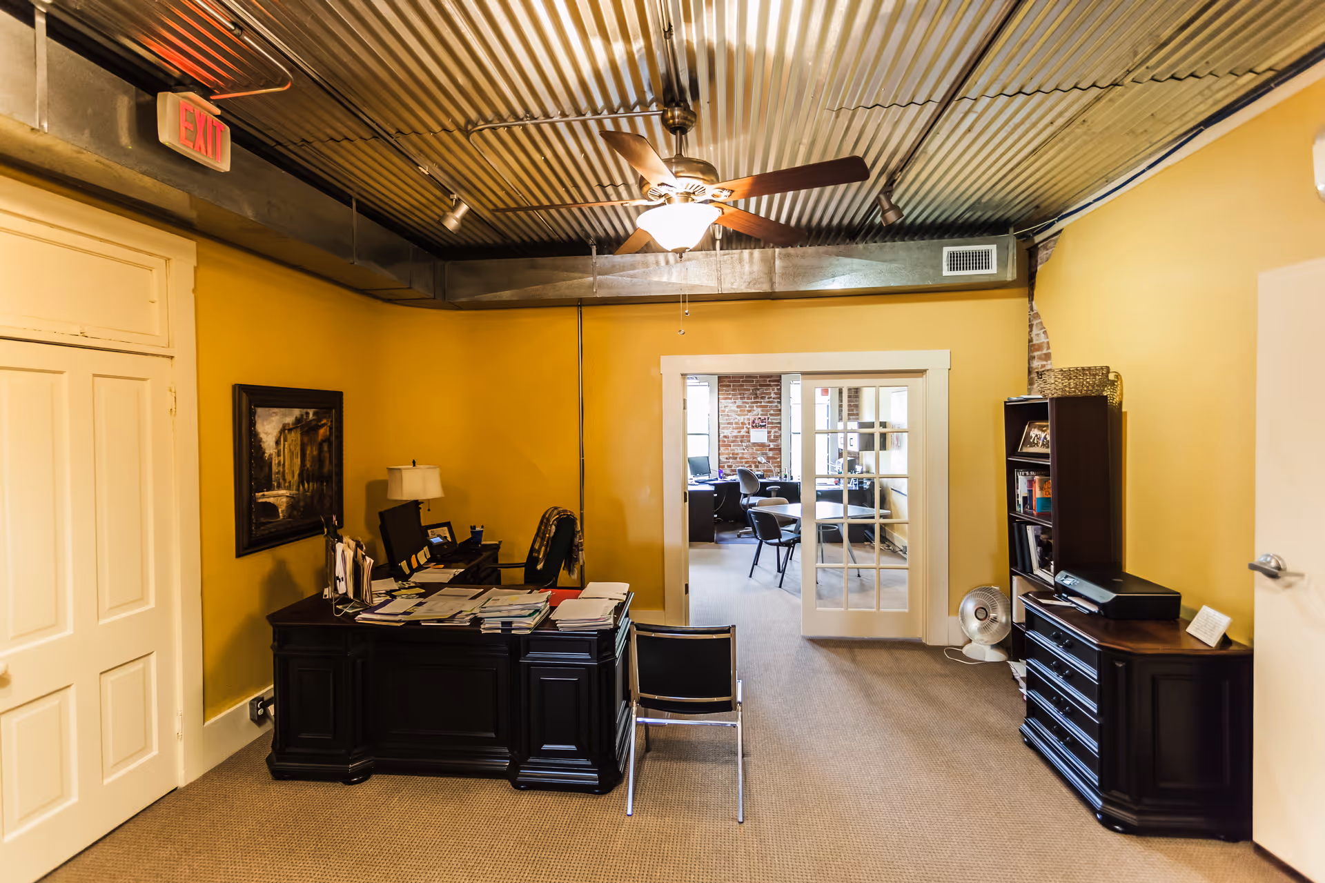 Yellow-walled reception area with a dark desk, seating, and French doors to another room.