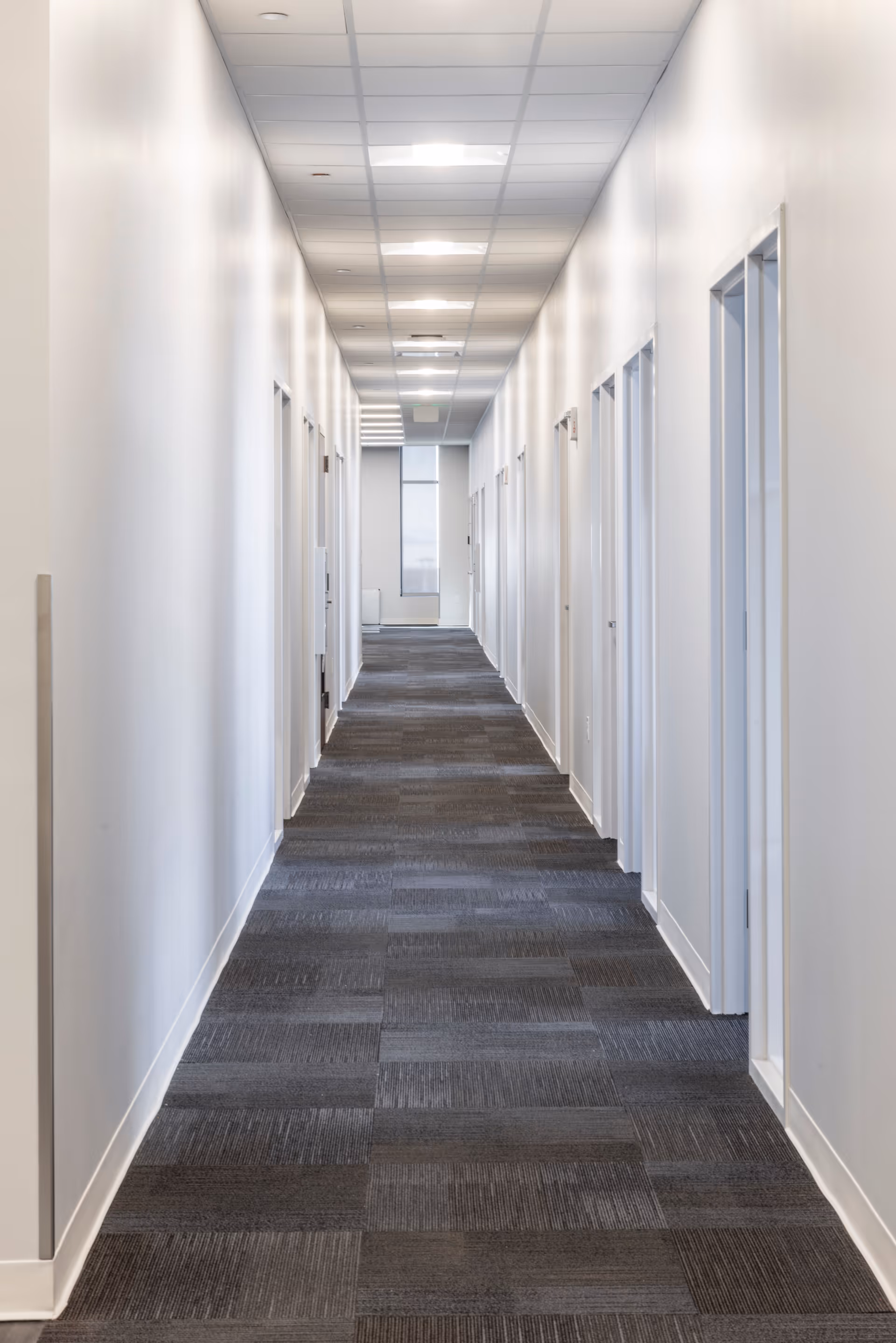 Long white corridor with doors on both sides and bright ceiling lights.