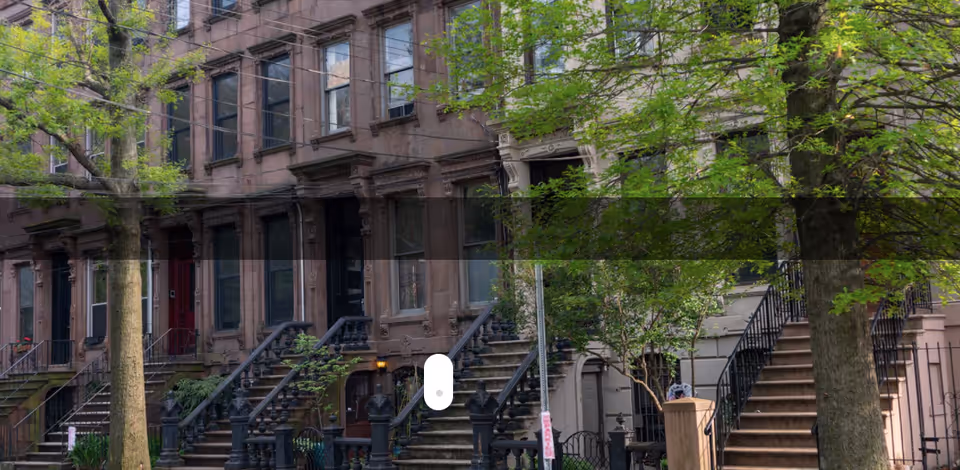 Exterior view of brownstone townhouses with front steps and green trees.