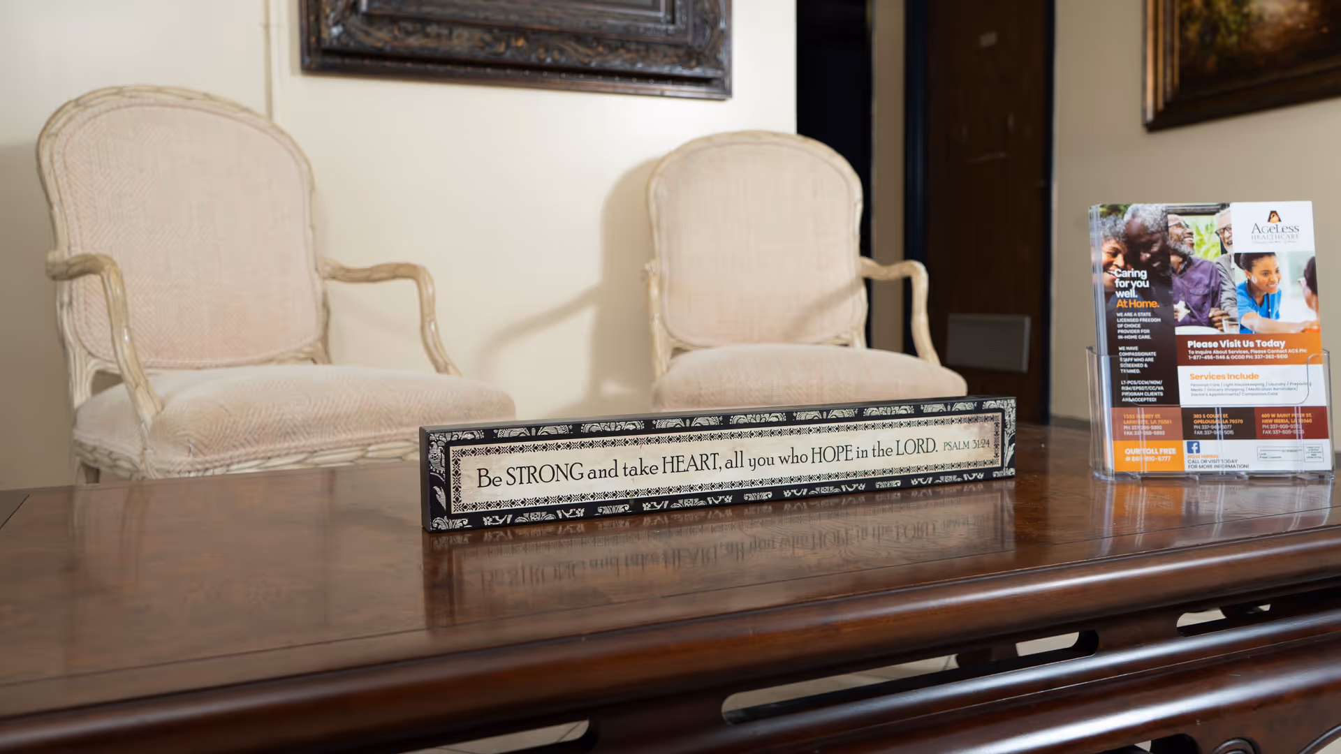 Two beige chairs behind a polished wooden reception table with a decorative sign and brochure.