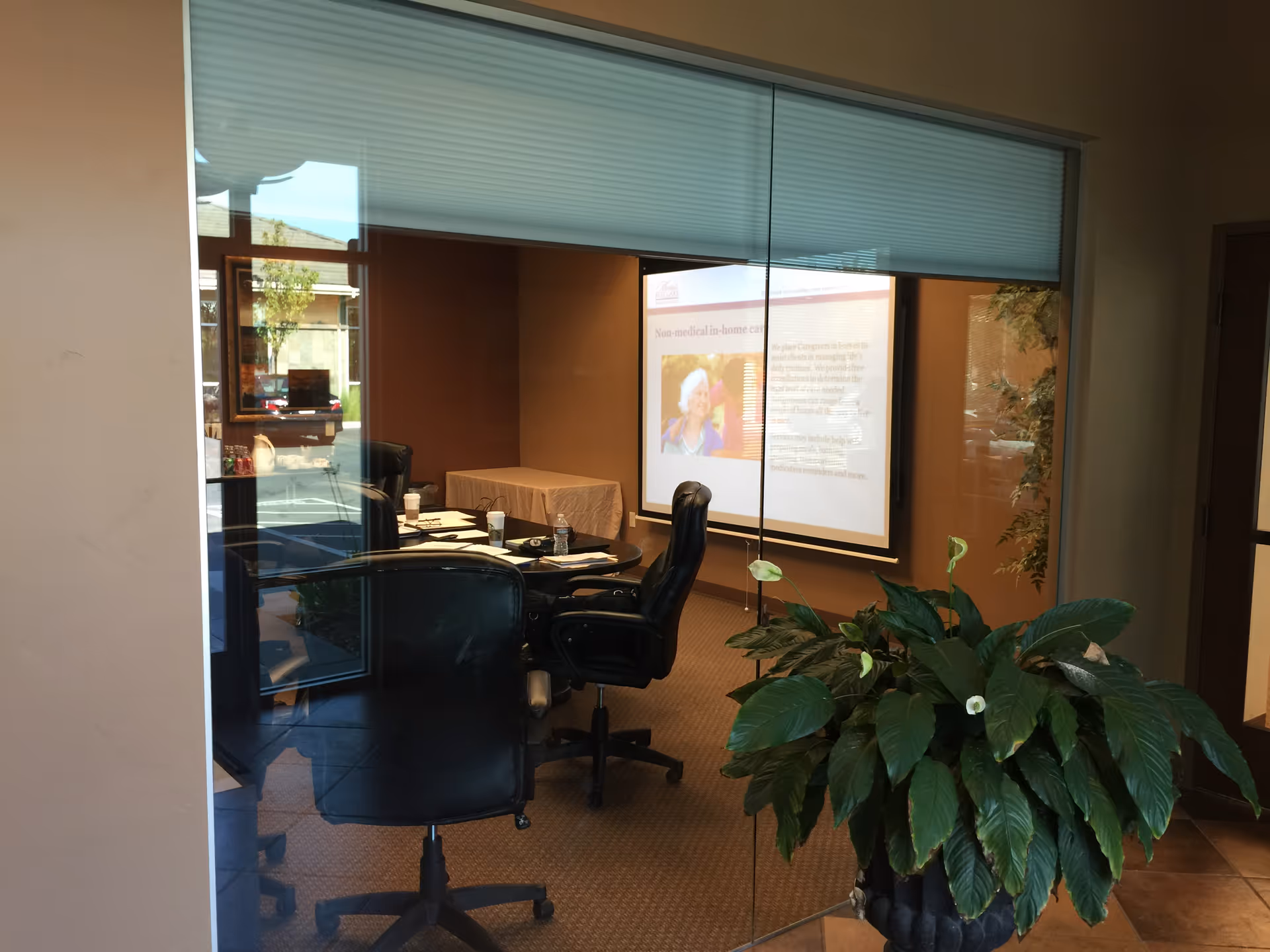 Glass-walled conference room with round table, projector, and potted plant.