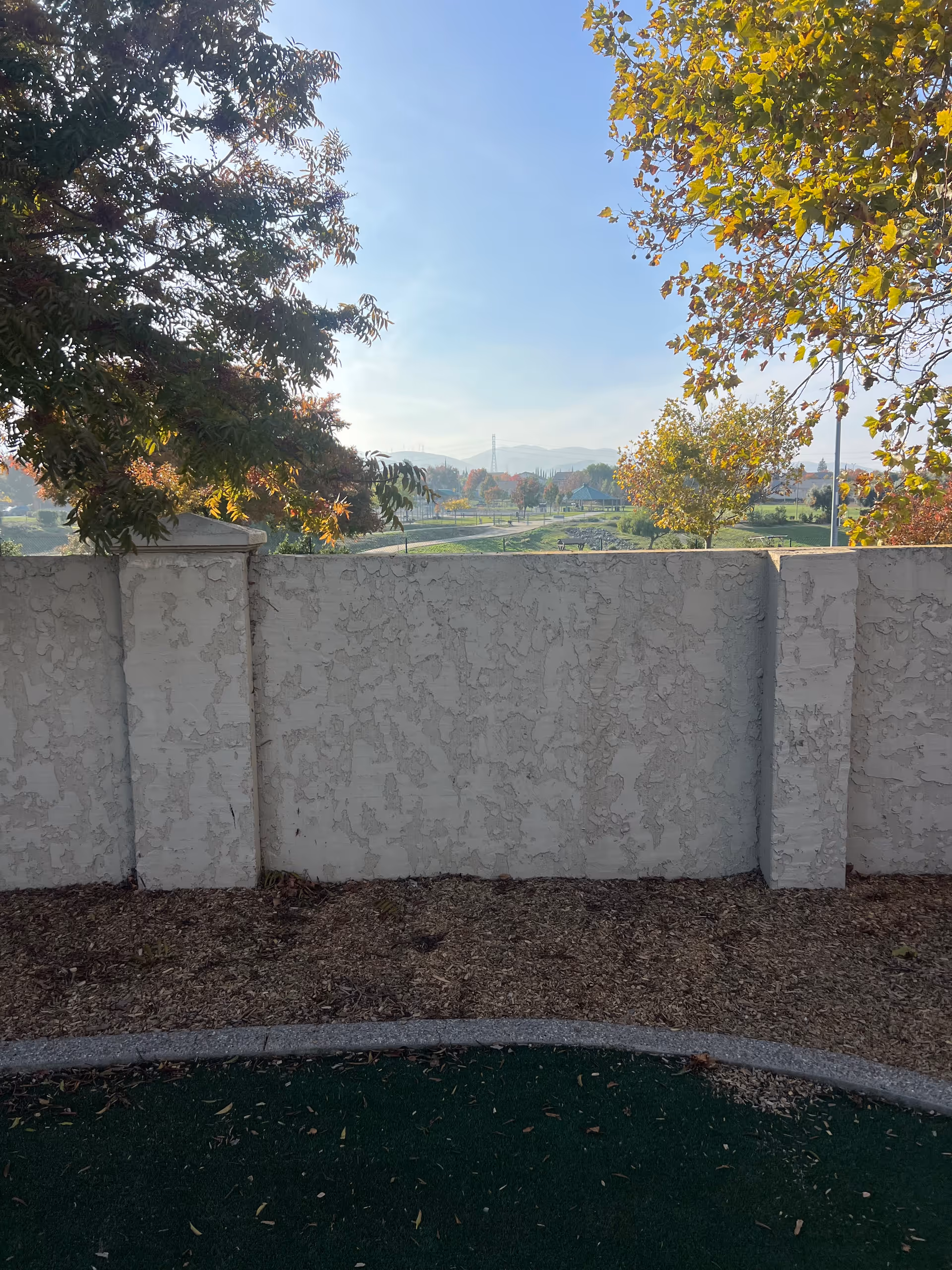 White textured concrete wall, outdoor courtyard, trees, and a distant town view.