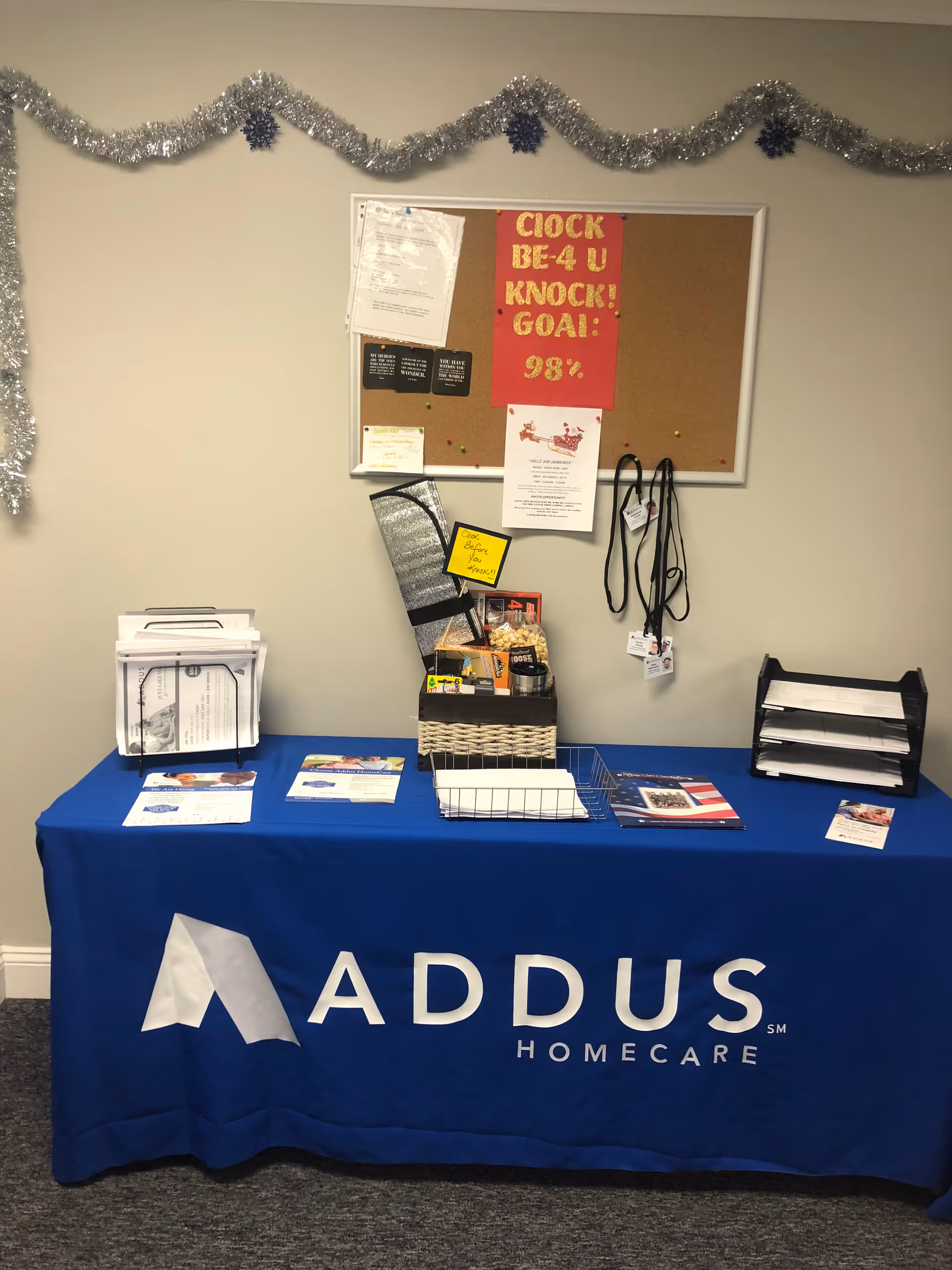 Info desk with ADDUS HomeCare table, bulletin board, and holiday garland.