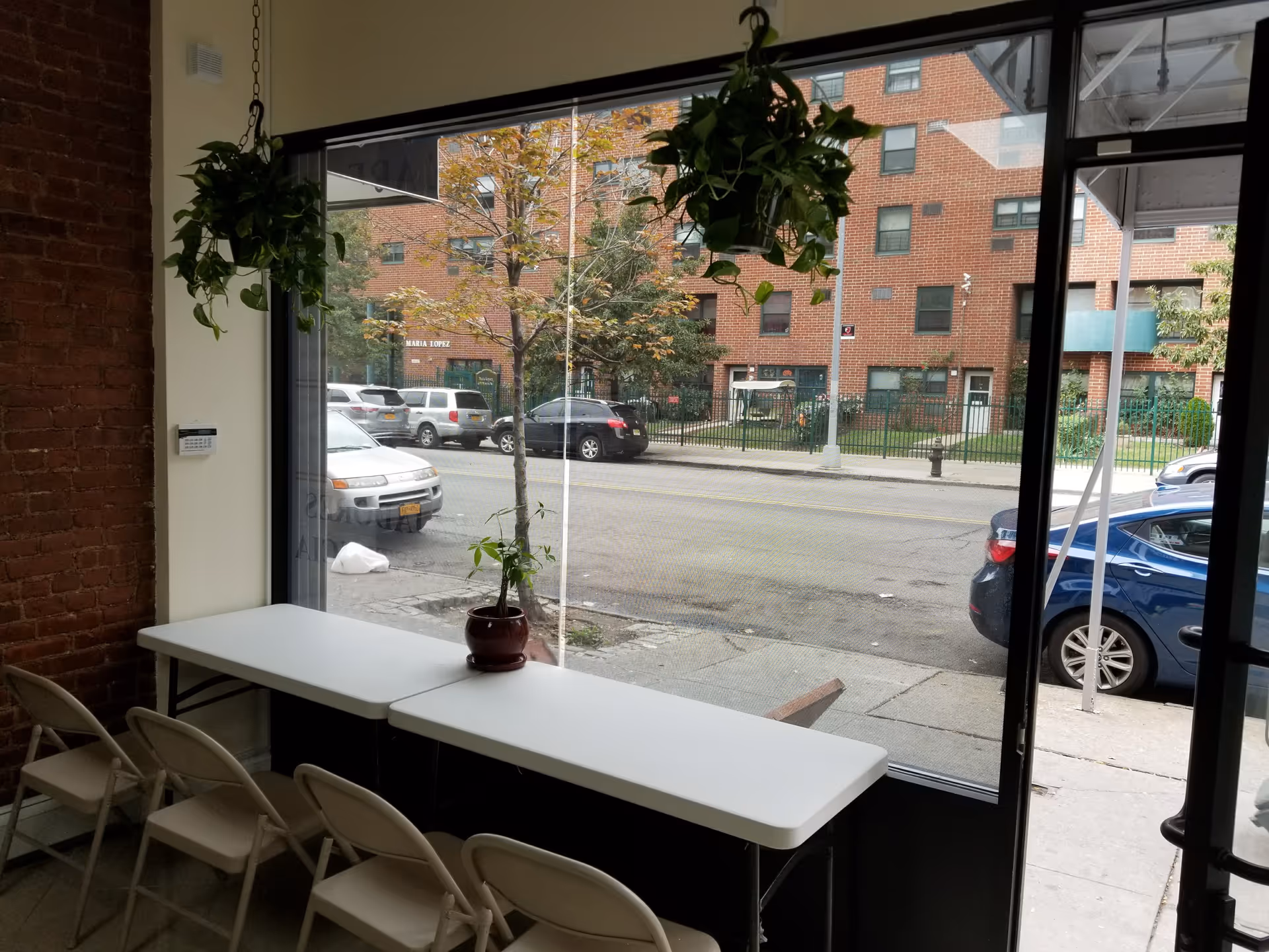Interior dining area with a long white table, folding chairs, and hanging plants.
