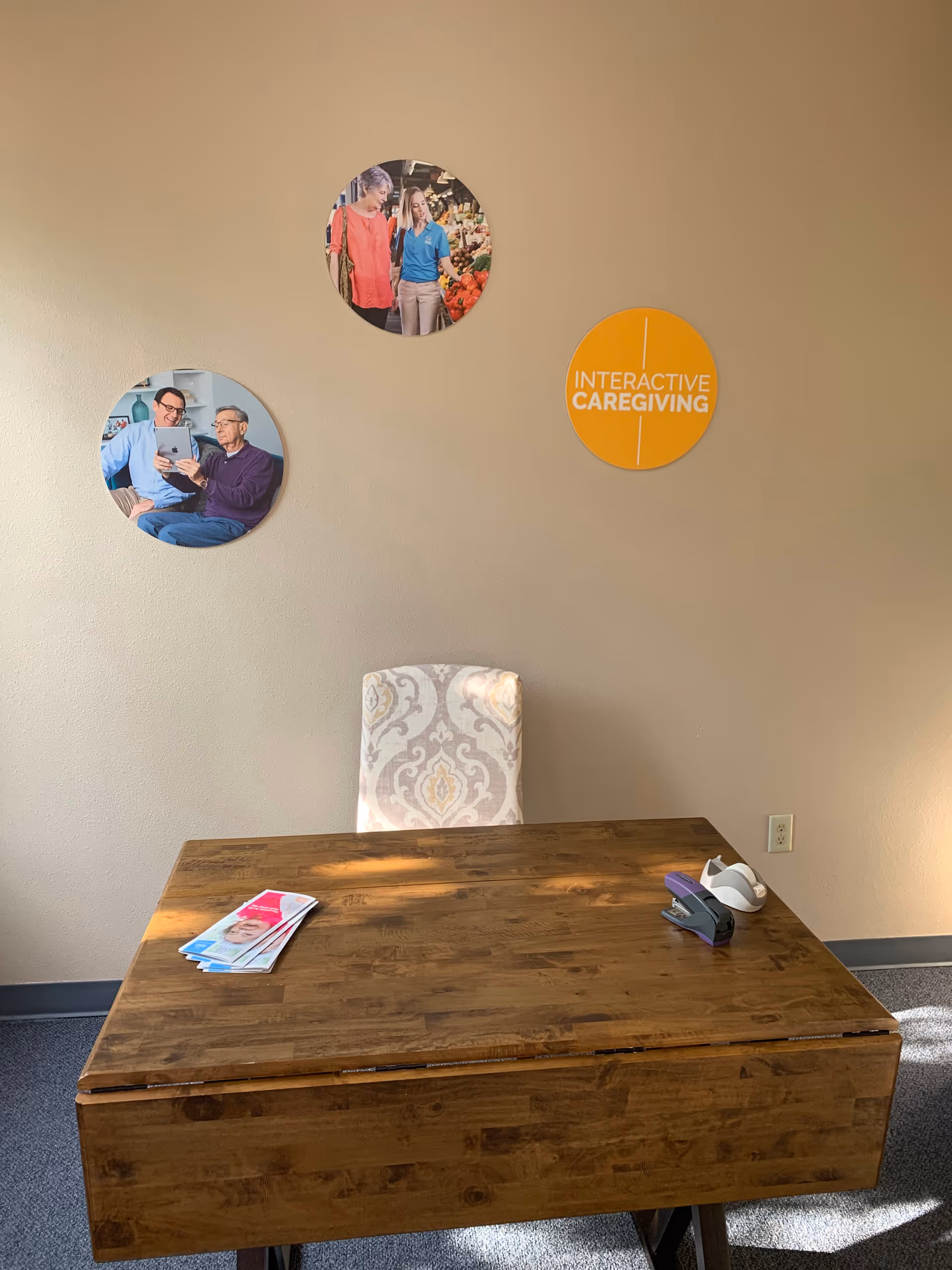 Wooden desk in beige-walled office with circular photos and interactive caregiving sign.