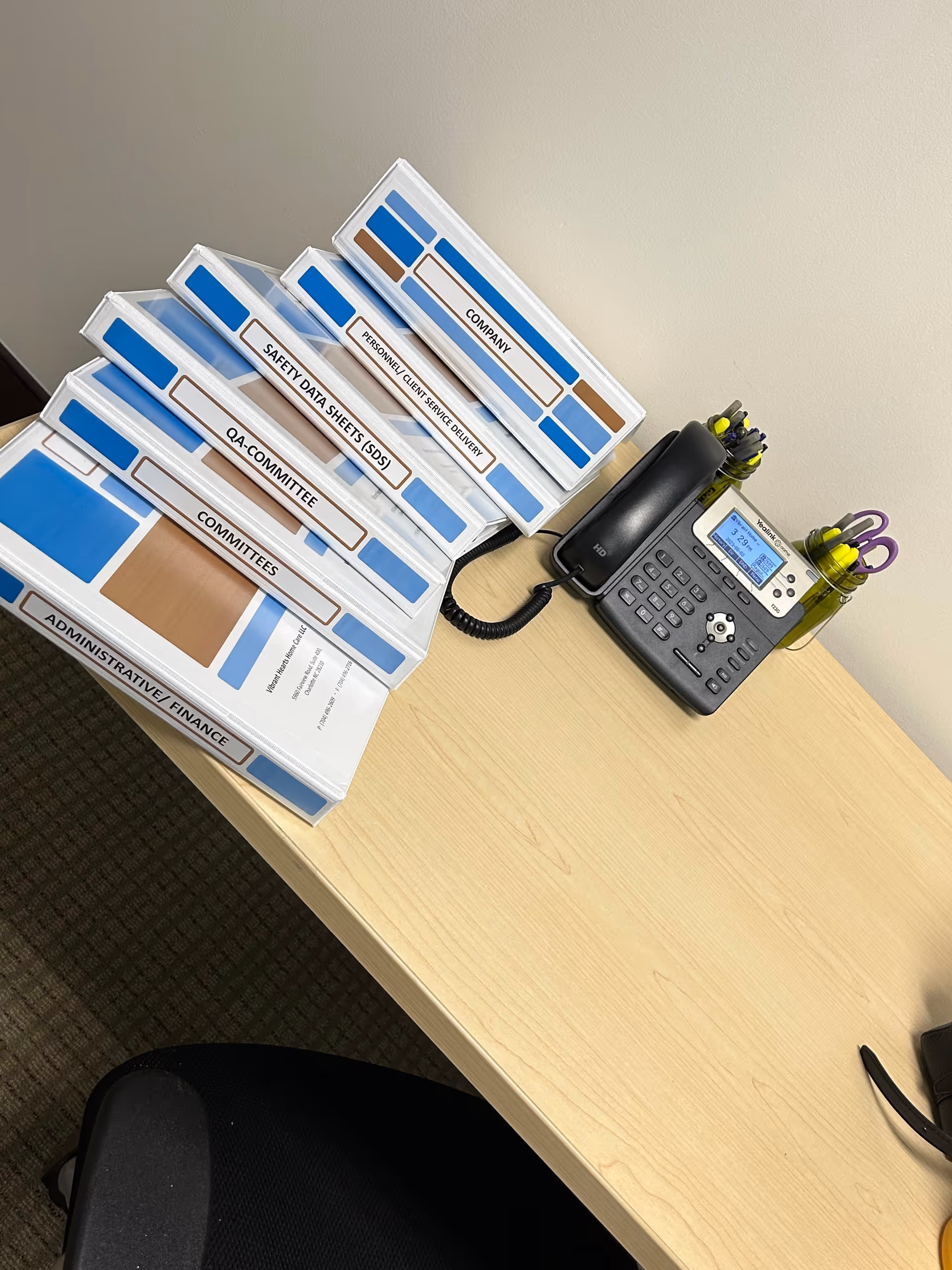 Office desk with stacked labeled folders and a desk phone in an administrative workspace.