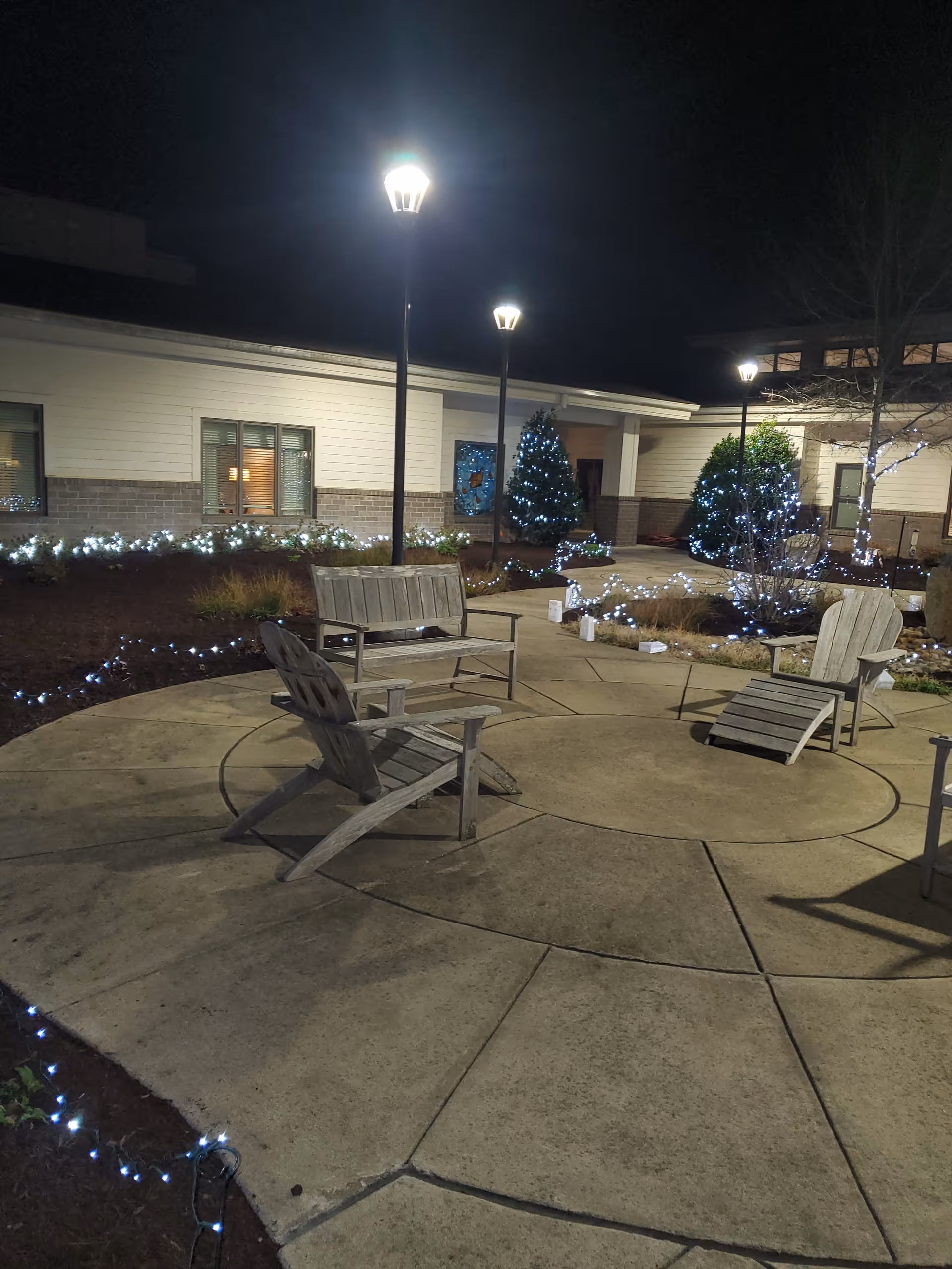Outdoor circular patio with wooden chairs, string lights, and a lit building in the background.